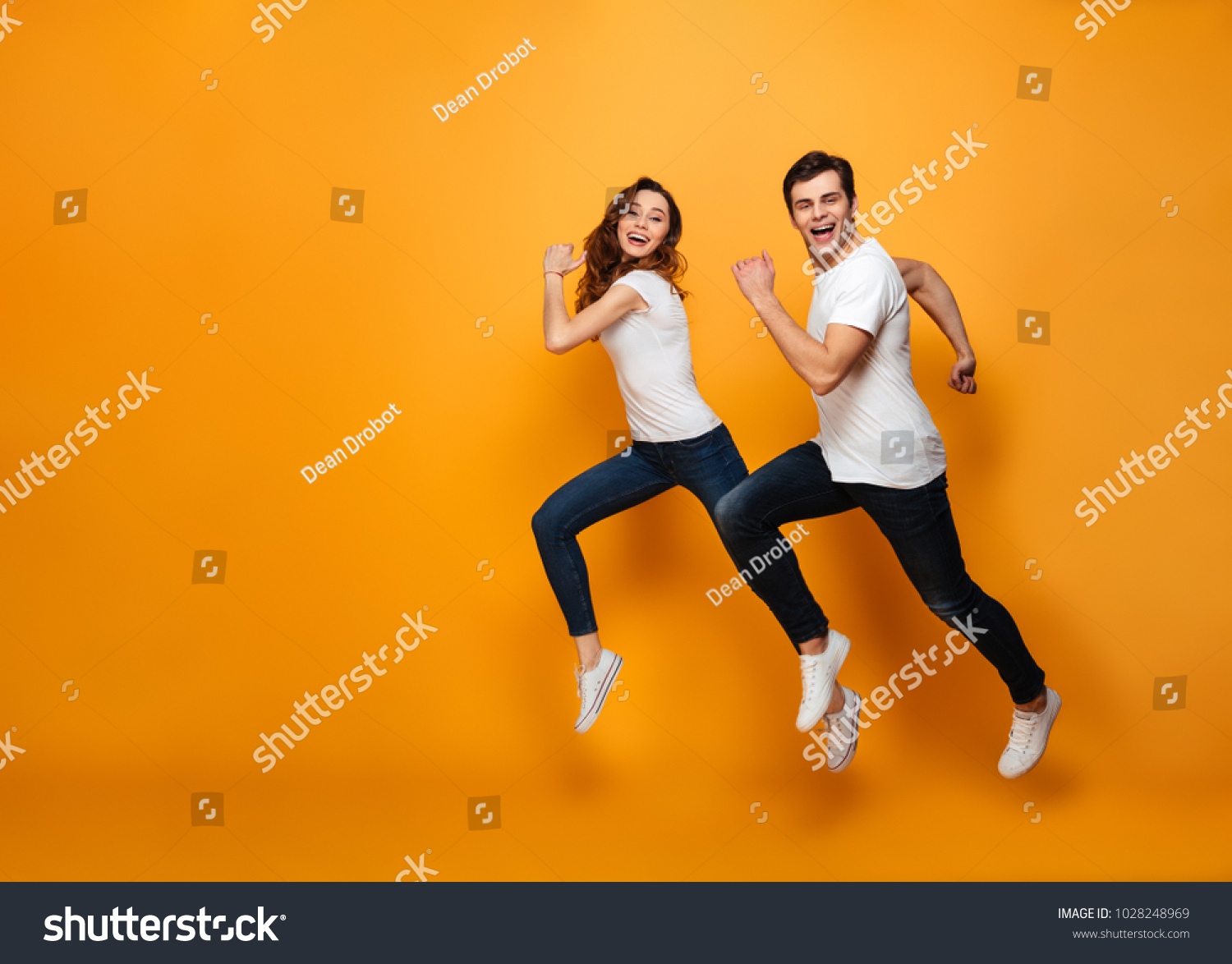 Young lovely cheerful couple posing together on camera while running or jumping along yellow background #1028248969