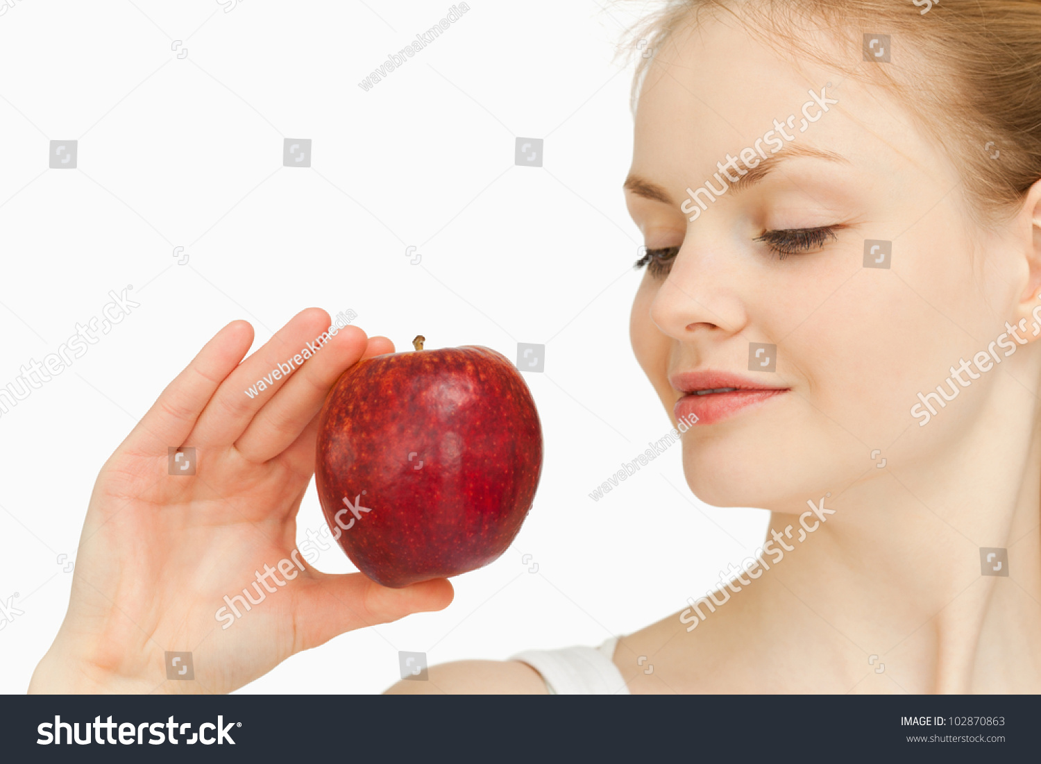 Woman holding an apple while looking at it against white background #102870863