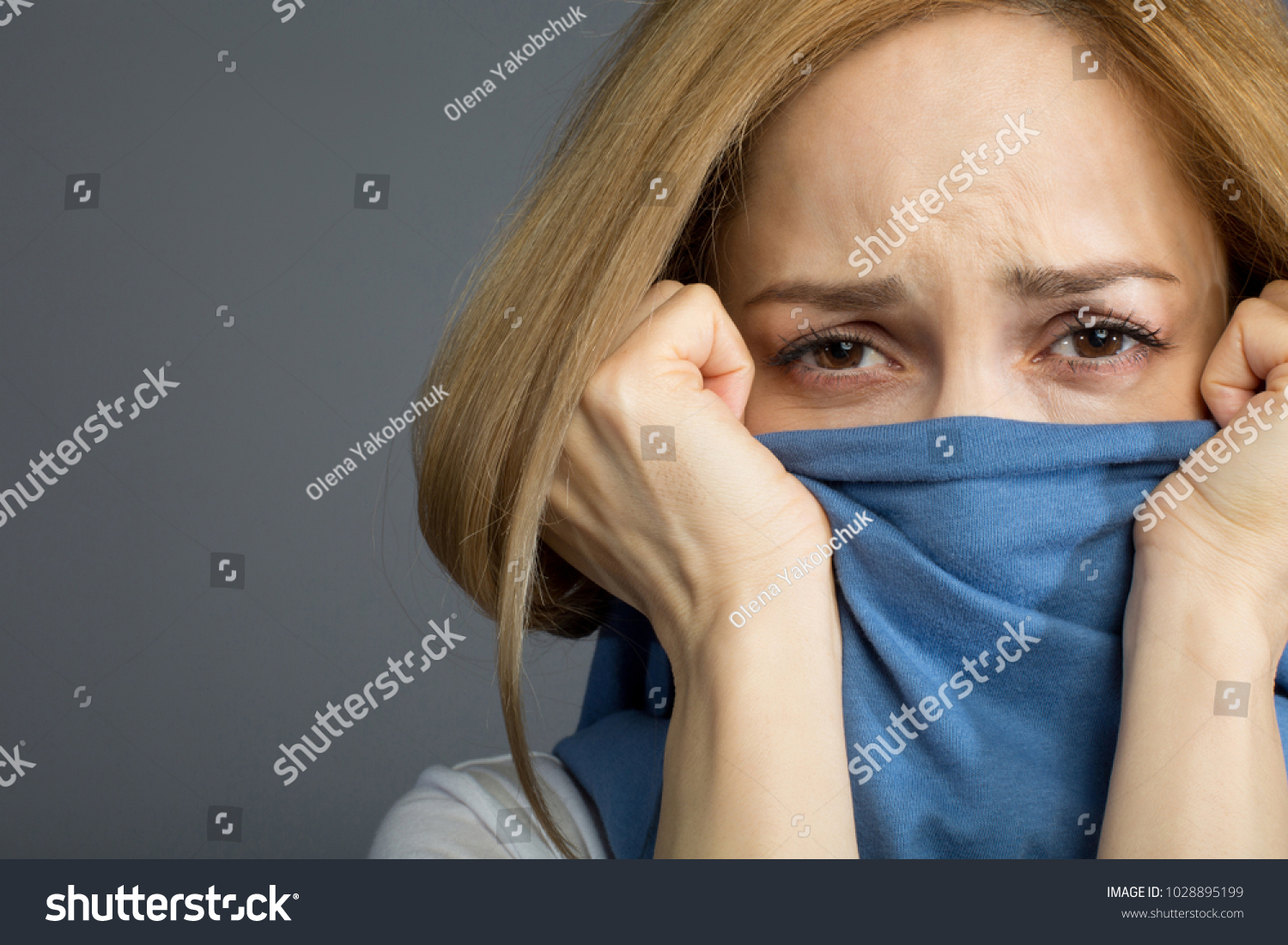 Protection concept. Depressed blonde lady covering her mouth with clothes and wrinkling her forehead expressing pain. Copy space in left side. Isolated on background #1028895199