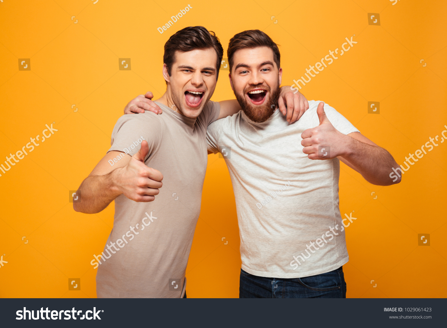 Portrait of a two happy young men showing thumbs up isolated over yellow background