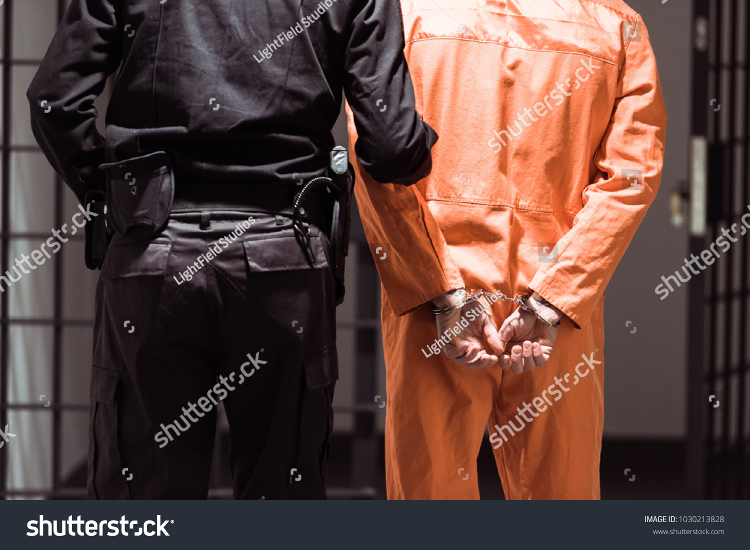 rear view of prison officer leading prisoner in handcuffs #1030213828