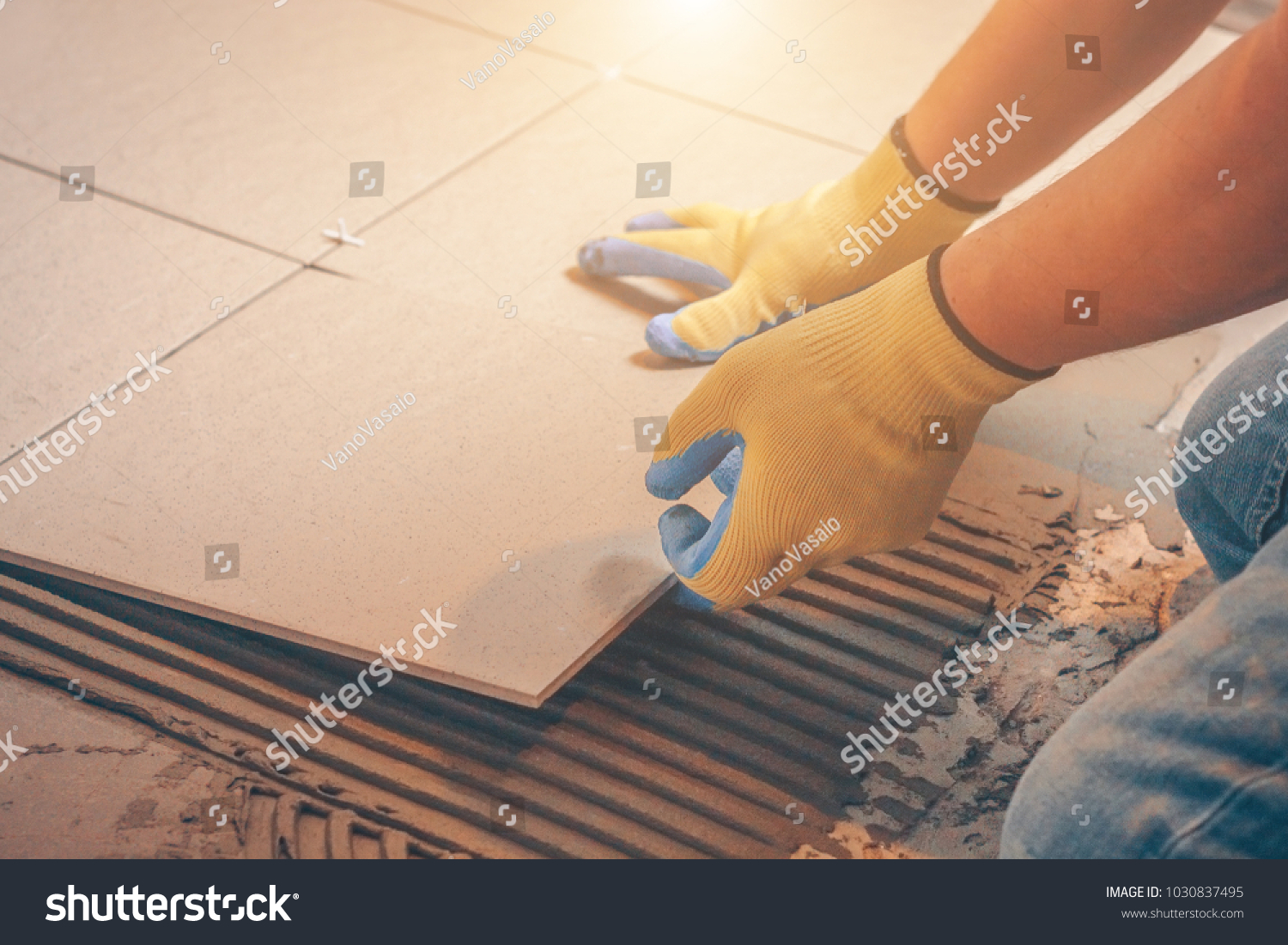 The tile glues the tile to the floor with a glue applied by a notched trowel #1030837495