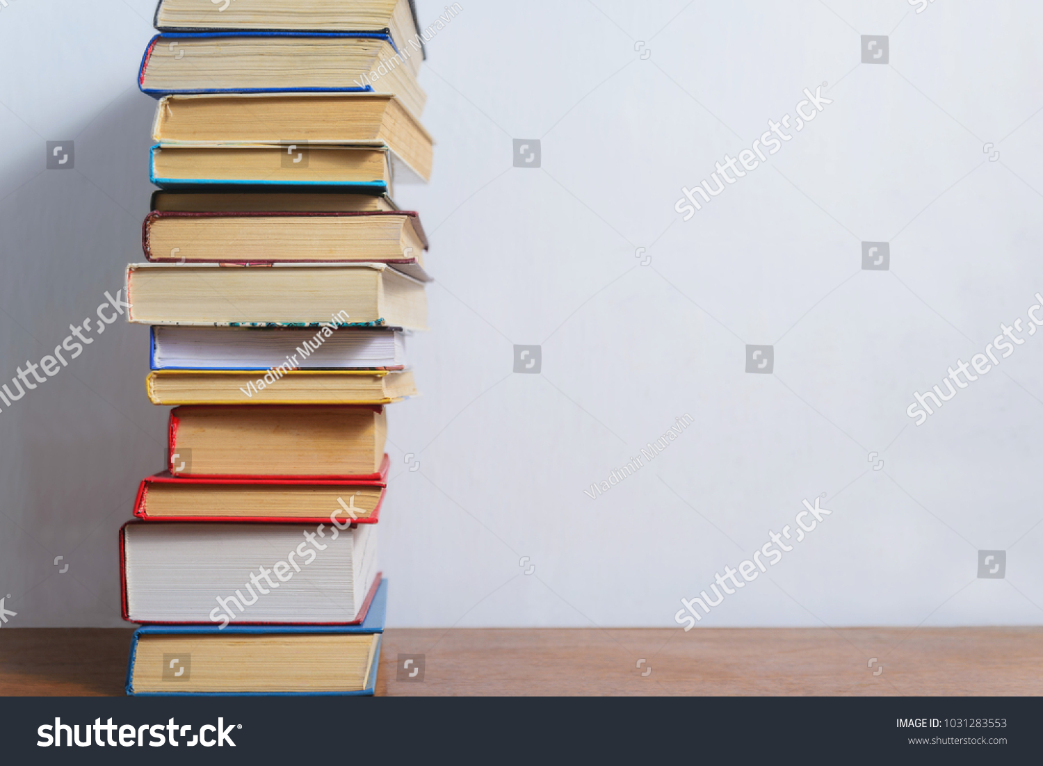 Stack of different books on a table against a white wall background #1031283553