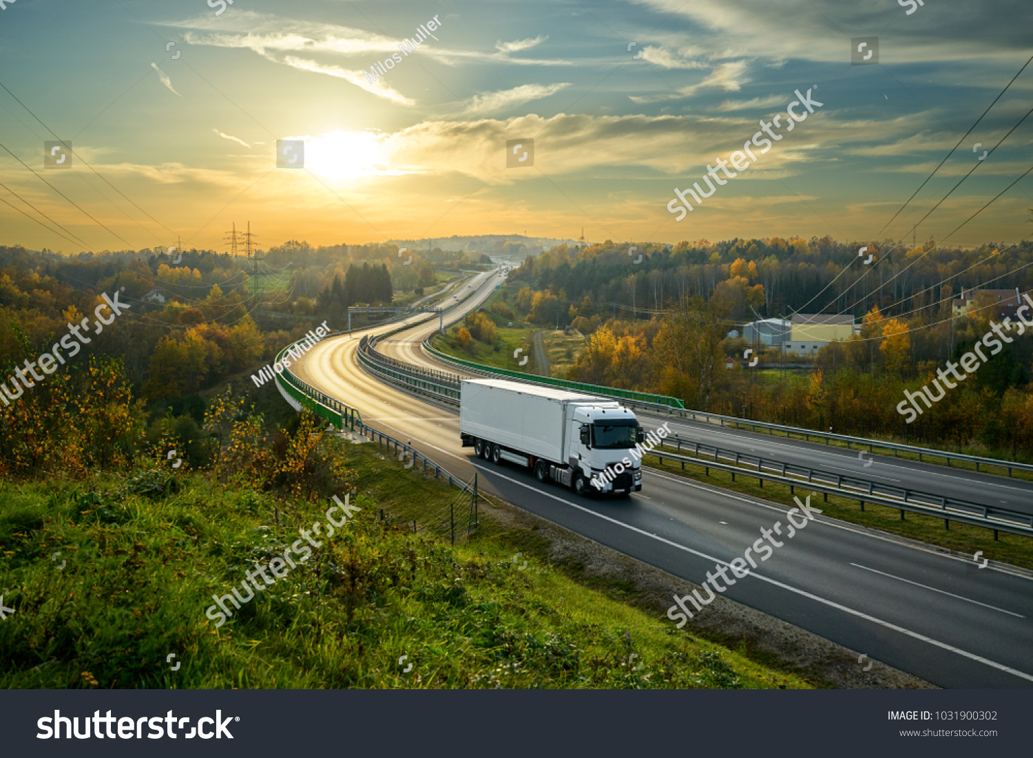 White truck driving on the highway winding through forested landscape in autumn colors at sunset #1031900302