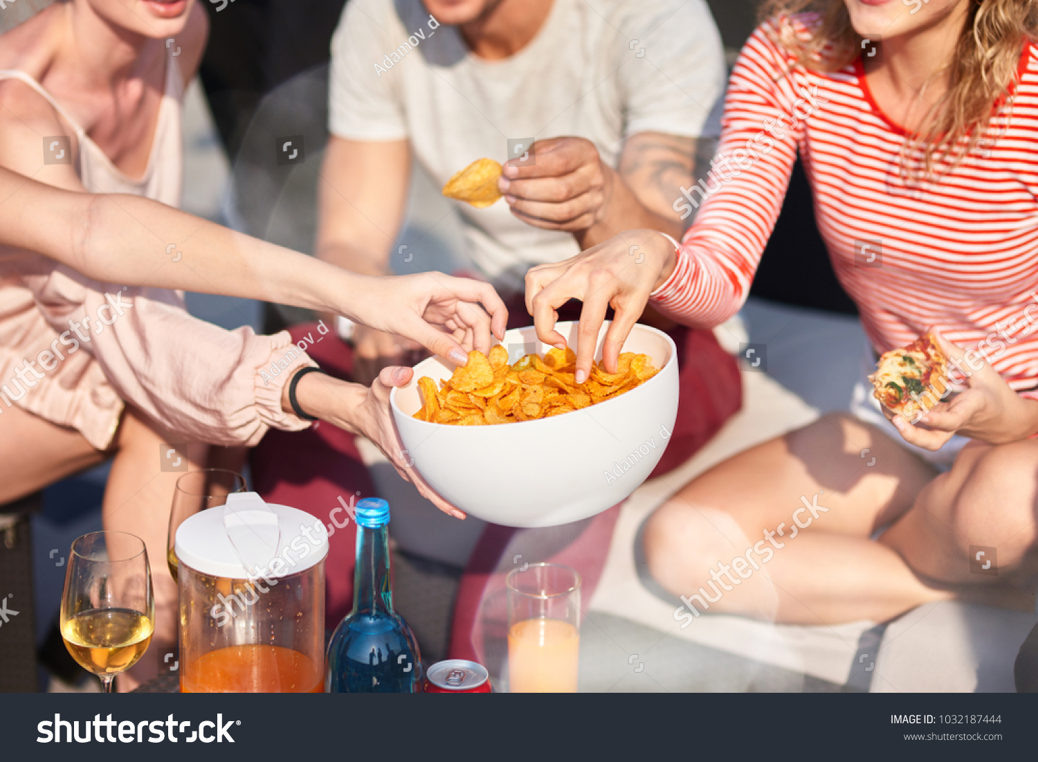 Enjoy it. Close up of bowl with snacks in hands of a young woman holding it while sharing with her friends #1032187444