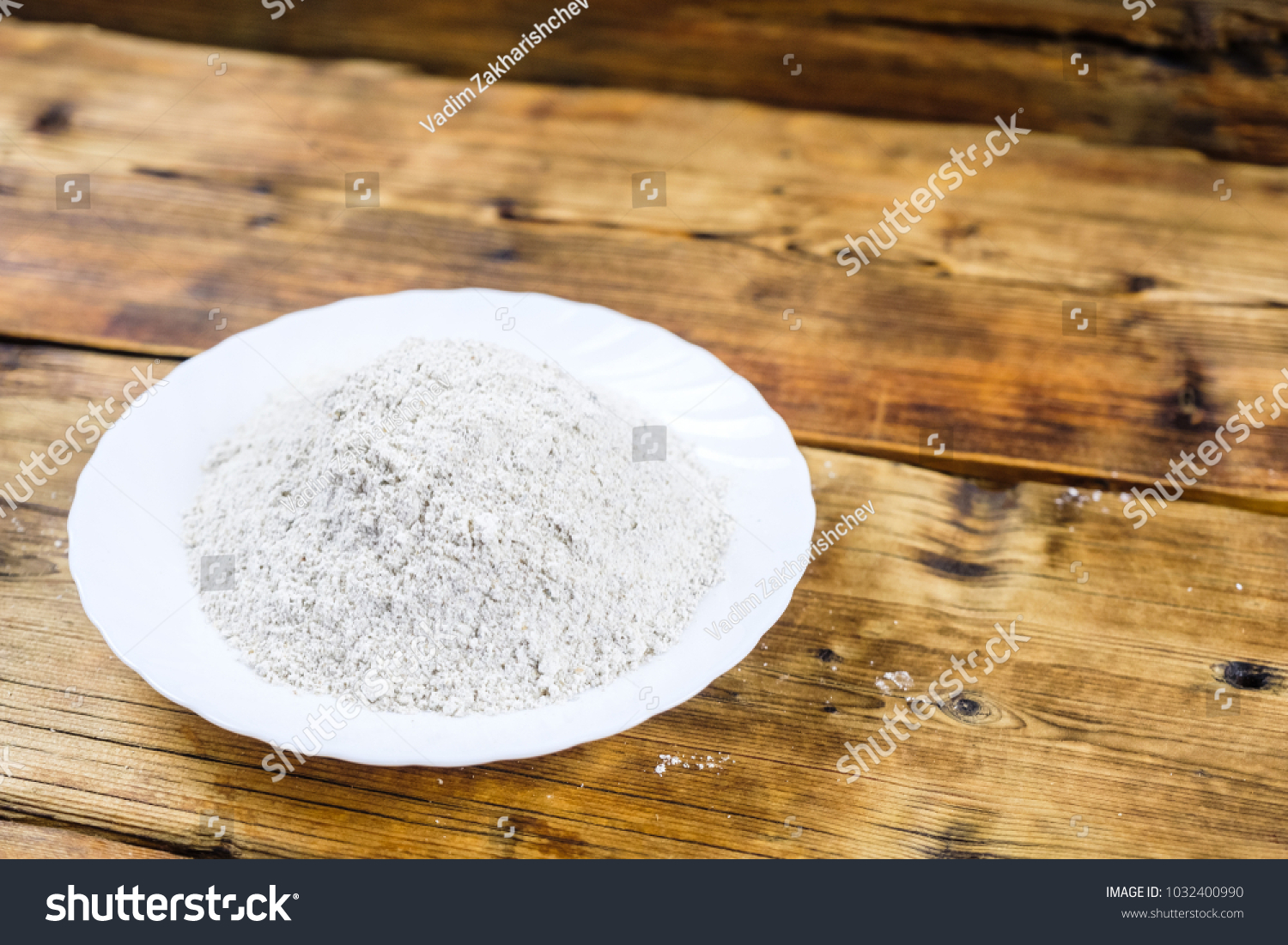 Close-up heap with wheat flour coarse in white plate on wooden background. Left on the photo #1032400990