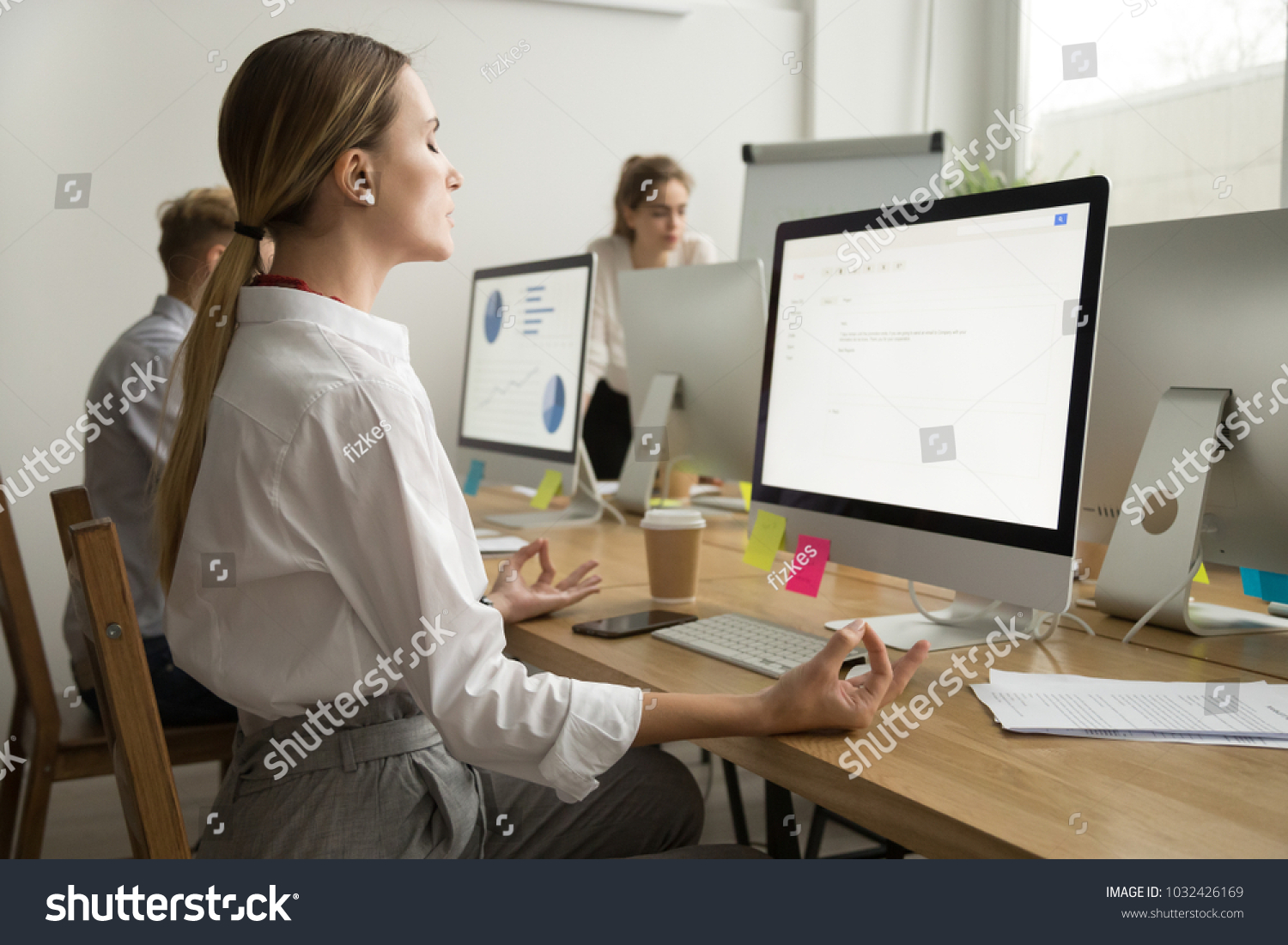 Calm peaceful young businesswoman meditating at office desk with eyes closed, company employee manager practicing yoga at workplace for mental emotional balance, no stress at work relief, side view #1032426169