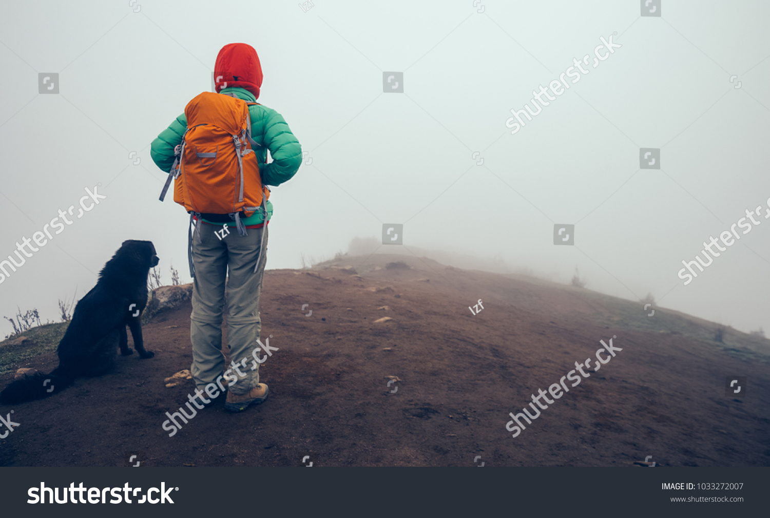 woman backpacker and dog on mountain top in bad weather #1033272007