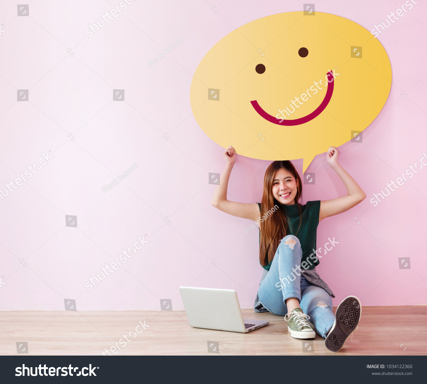Happy Customer Concept. Review and Feedback her Experience for Satisfaction Survey Online. Young Female in Cheerful Posture, Raise up Speech Bubble with Smiley Face. Sit on the Floor with Laptop #1034122360