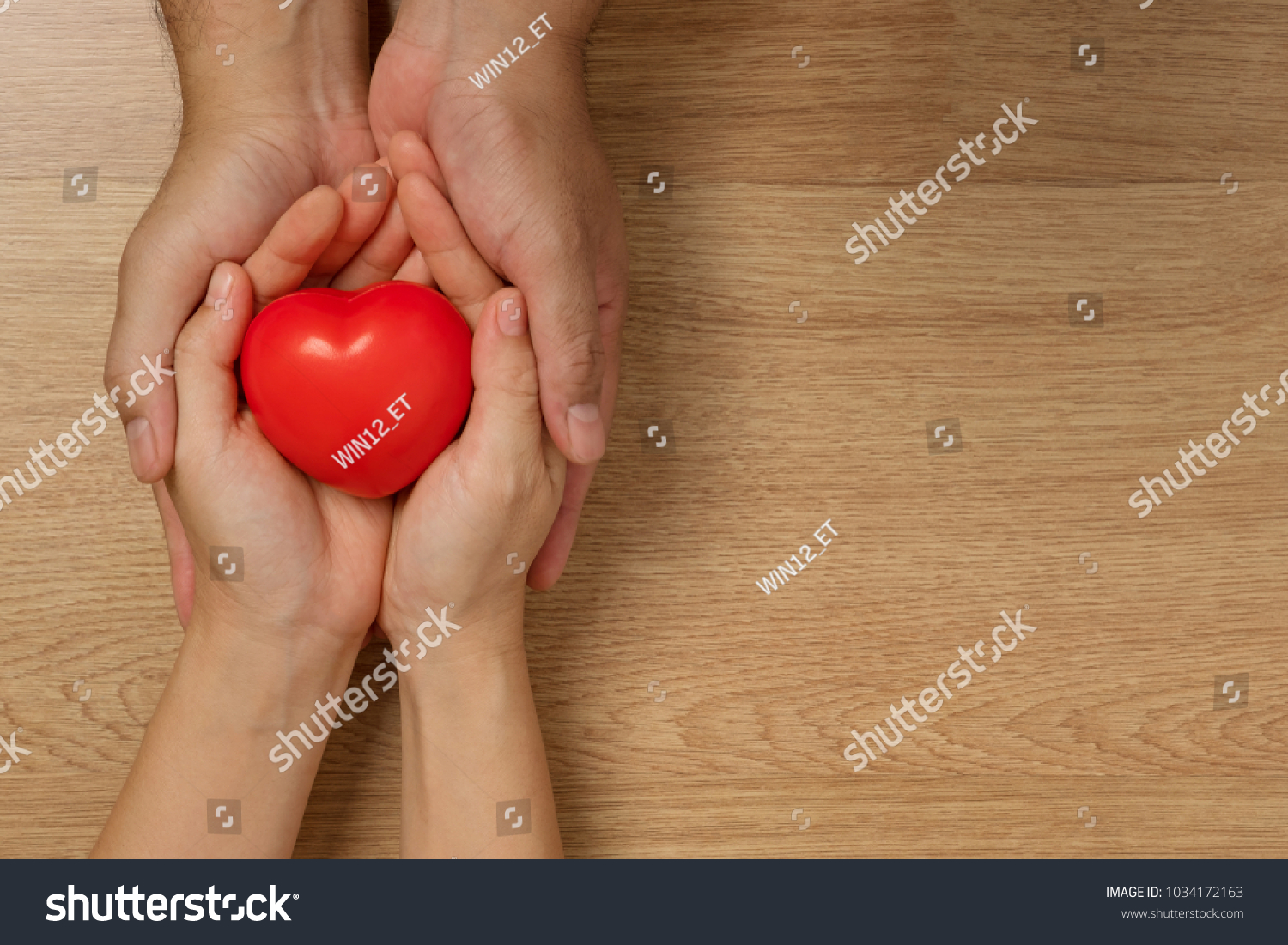 Concept of love in Valentine's Day. Hands of men and women holding red heart to give love on a wooden floor. #1034172163