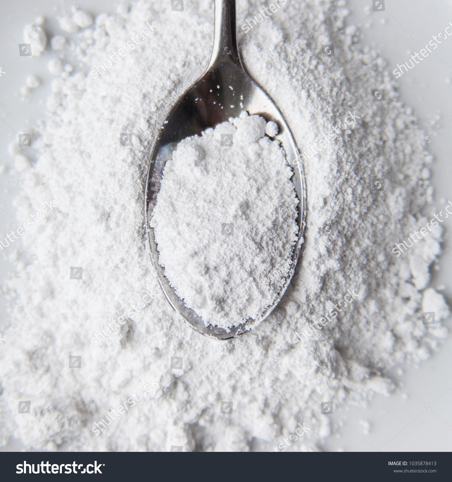 White powder in silver spoon over white background. Top view. Detailed close-up shot. Icing, caster, confectioners or powdere sugar pile. #1035878413