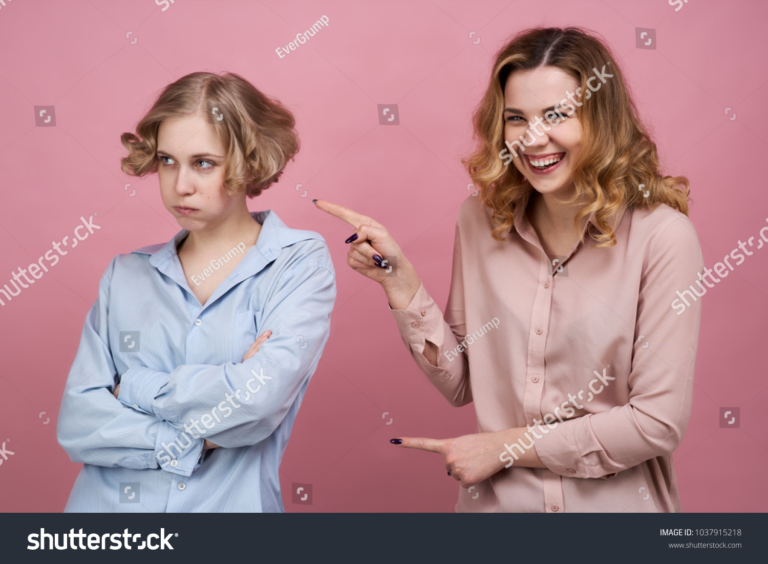 Two young girls pose for a Studio portrait on isolated background. One of them laughs and has fun mocking the failure of the other. The concept of trolling to be bullying and friendships #1037915218