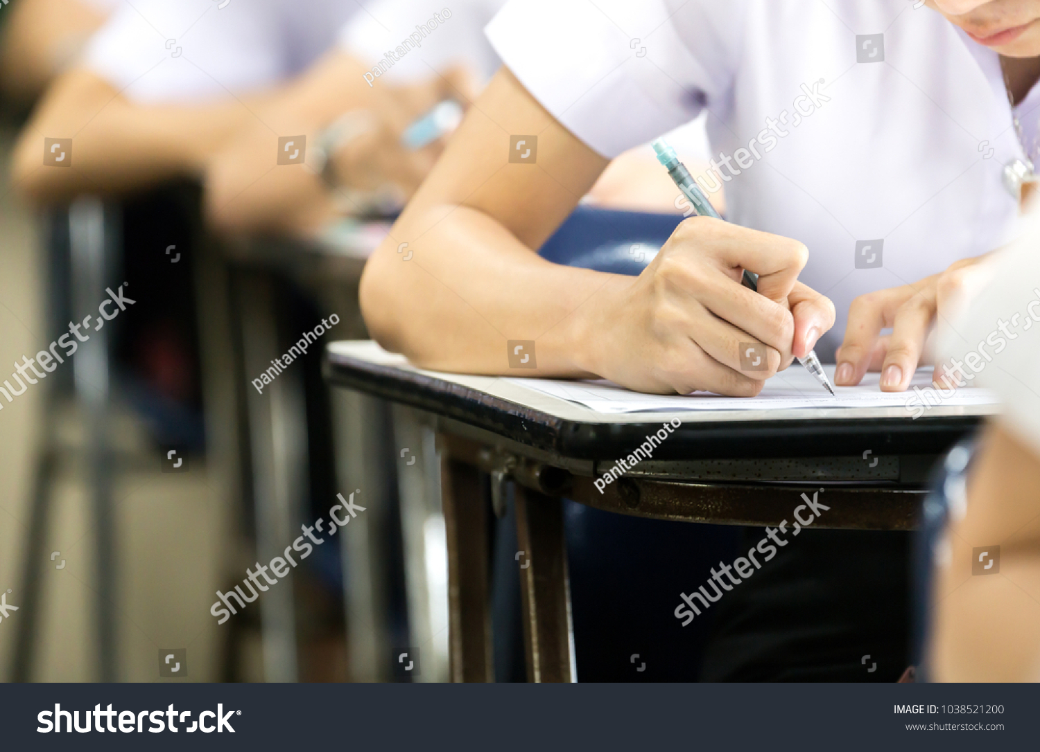 soft focus.high school or university student holding pencil writing on paper answer sheet.sitting on lecture chair taking final exam attending in examination room or classroom.student in uniform #1038521200
