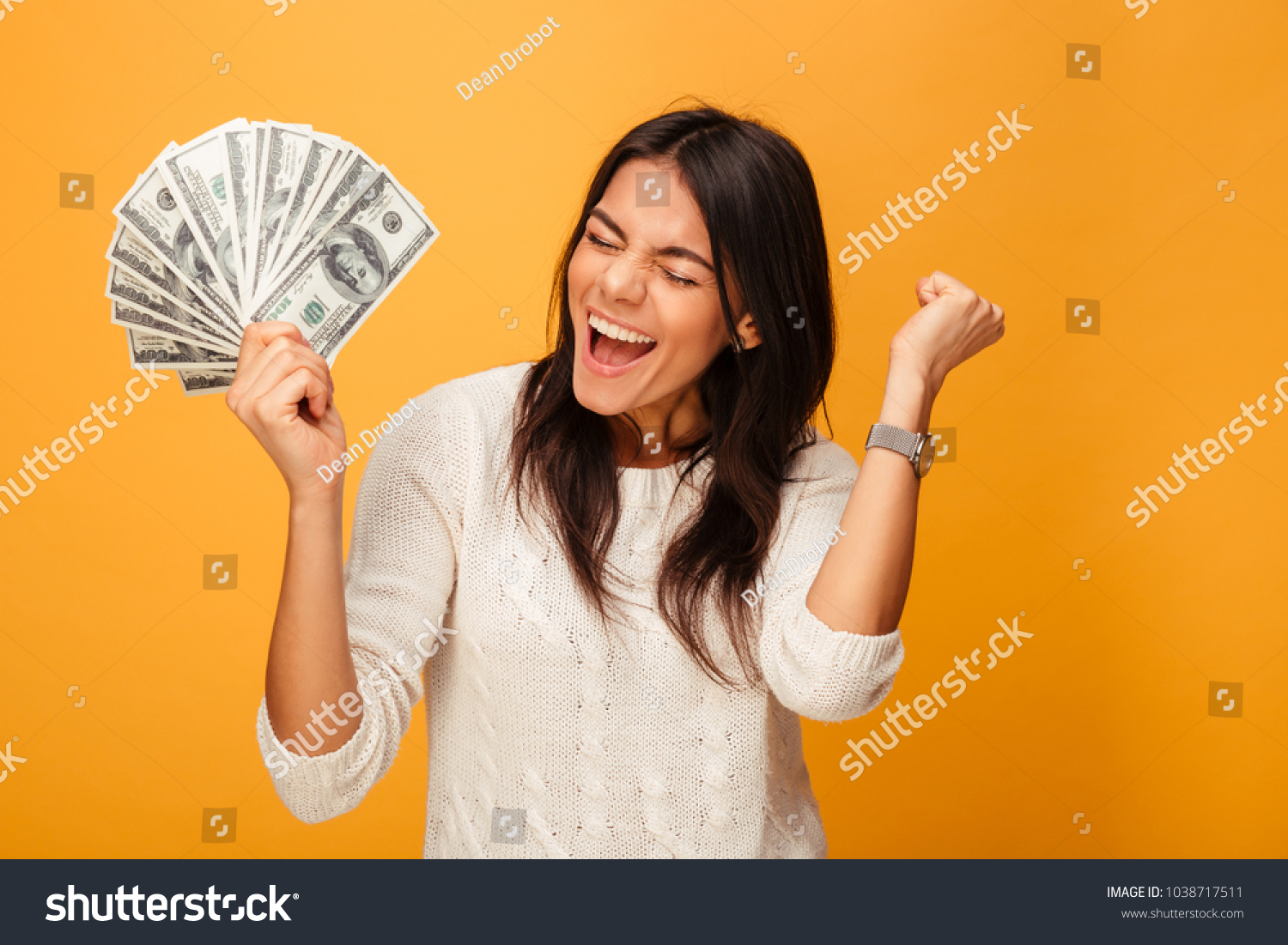 Portrait of a cheerful young woman holding money banknotes and celebrating isolated over yellow background #1038717511