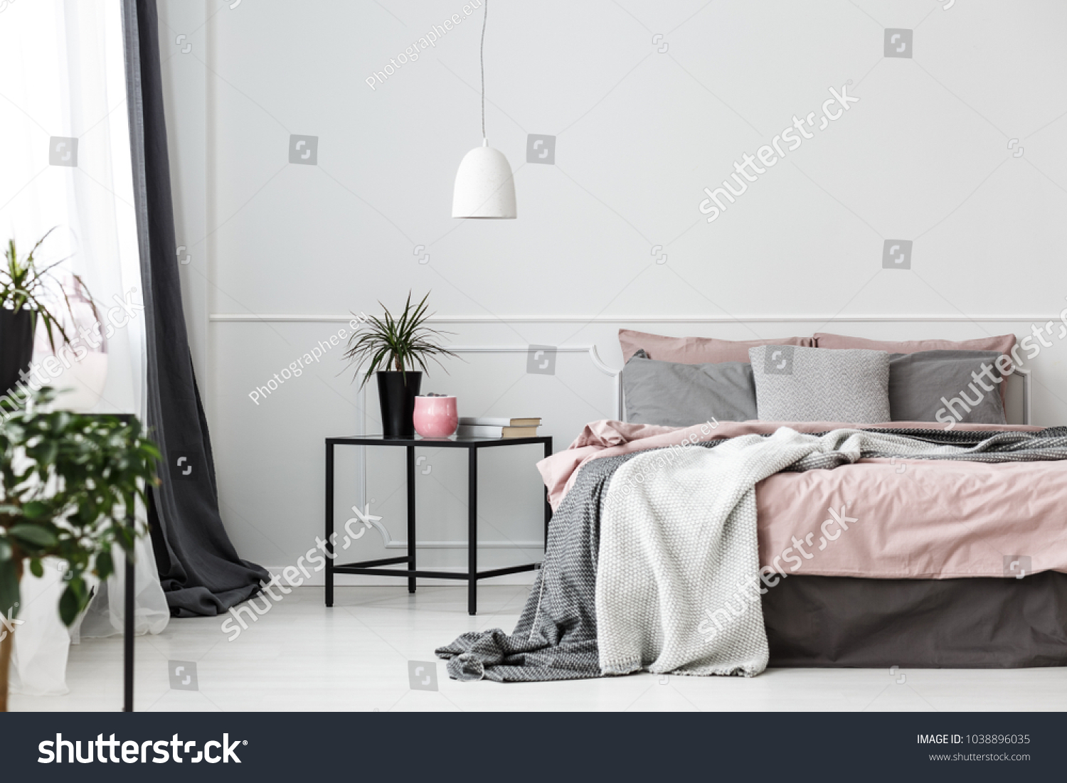 Grey bedsheets on bed in pink bedroom interior with plant on the table against white wall #1038896035
