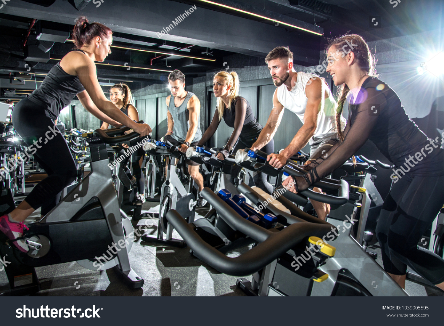 Group of sporty women and men training on exercise bikes together at gym. #1039005595