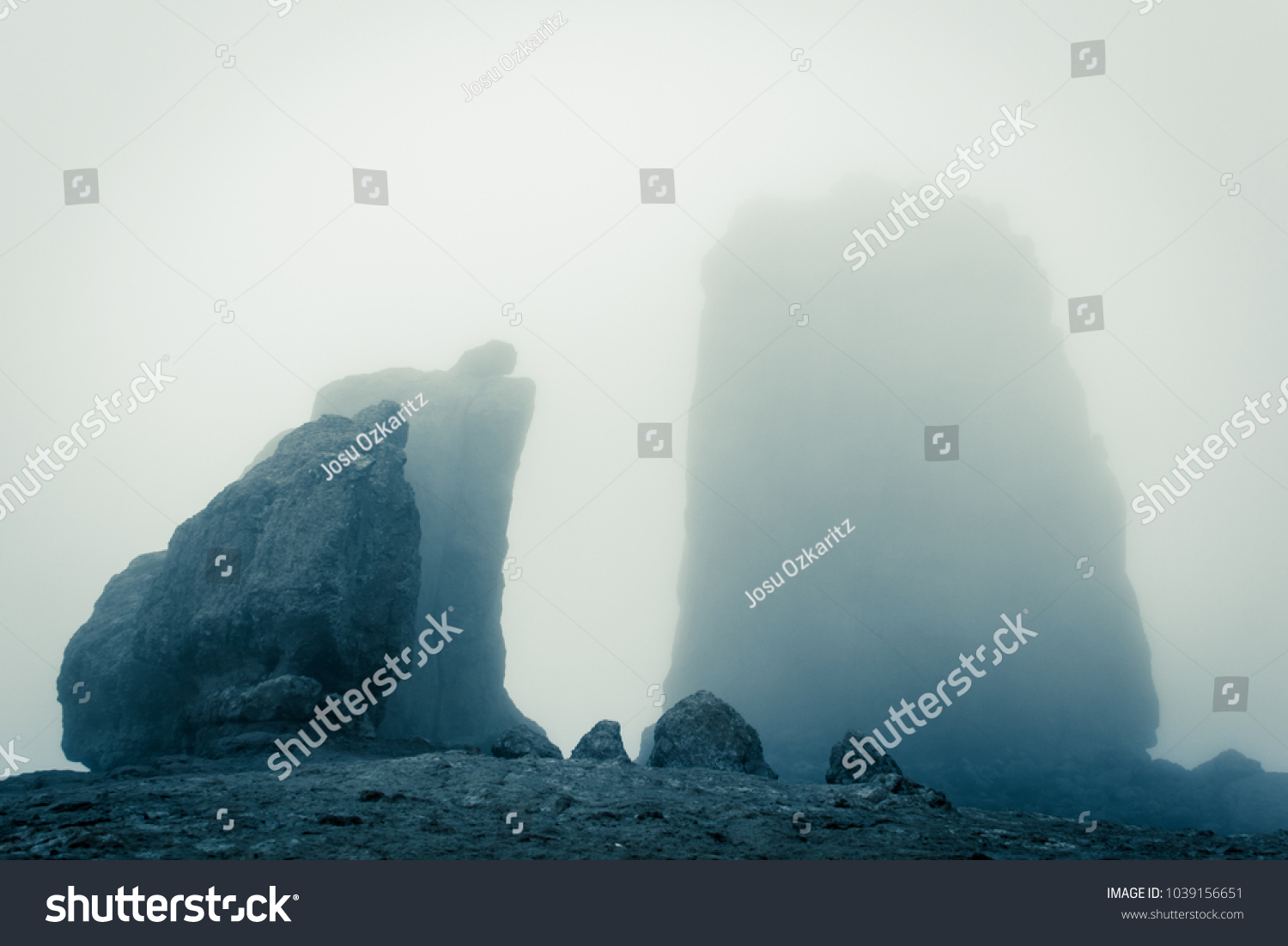 Roque Nublo big rock mountain covered with heavy fog in Gran Canaria, Spain. Futuristic sci fi landscape setting. Thriller, mysterious empty space. Blue effect #1039156651