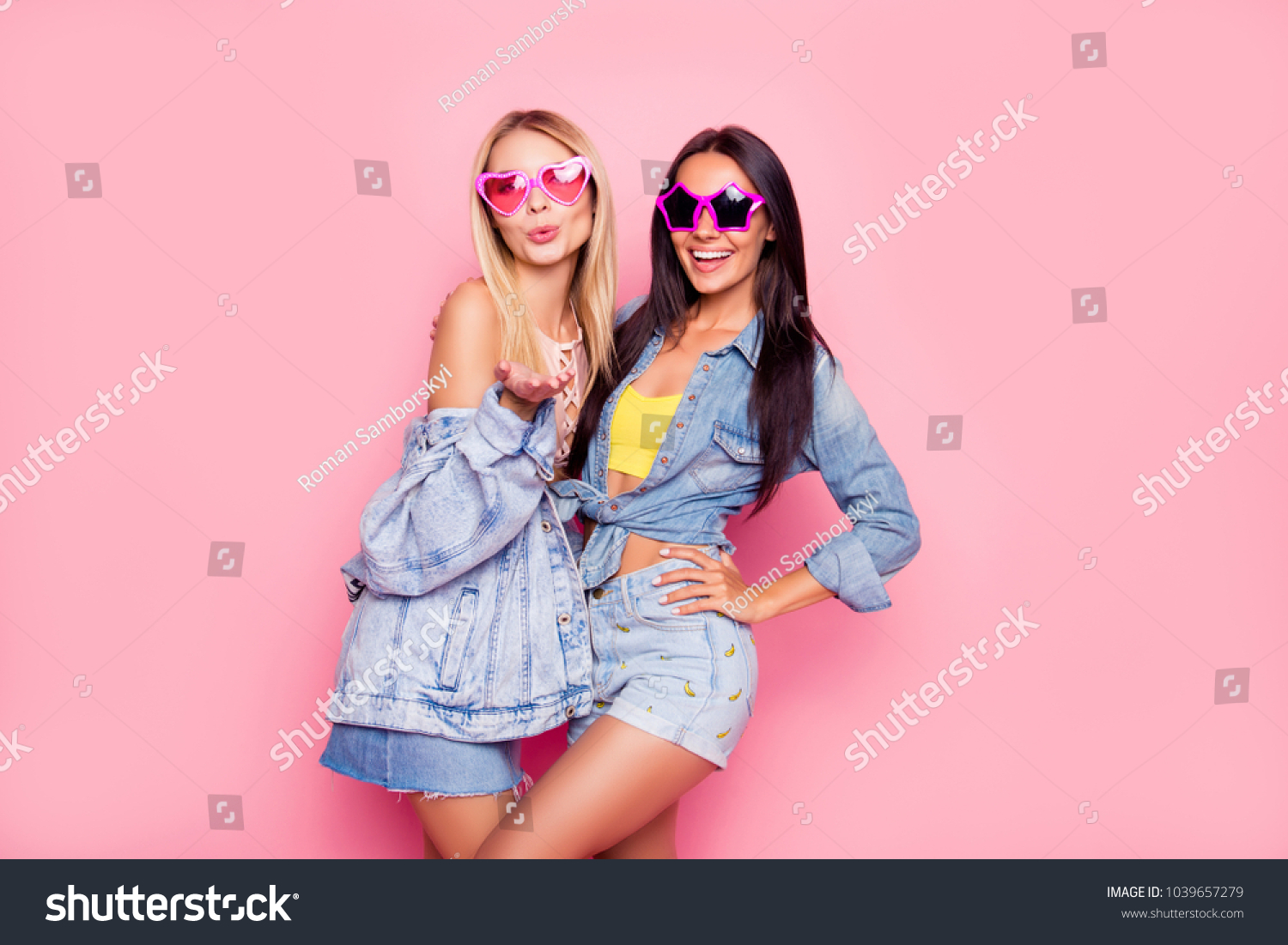 I like you! Beautiful playful cheerful women dressed in fashionable stylish shorts, shirt, jacket, top, funny star and heart glasses are embracing, sending air-kiss, isolated on bright pink background #1039657279