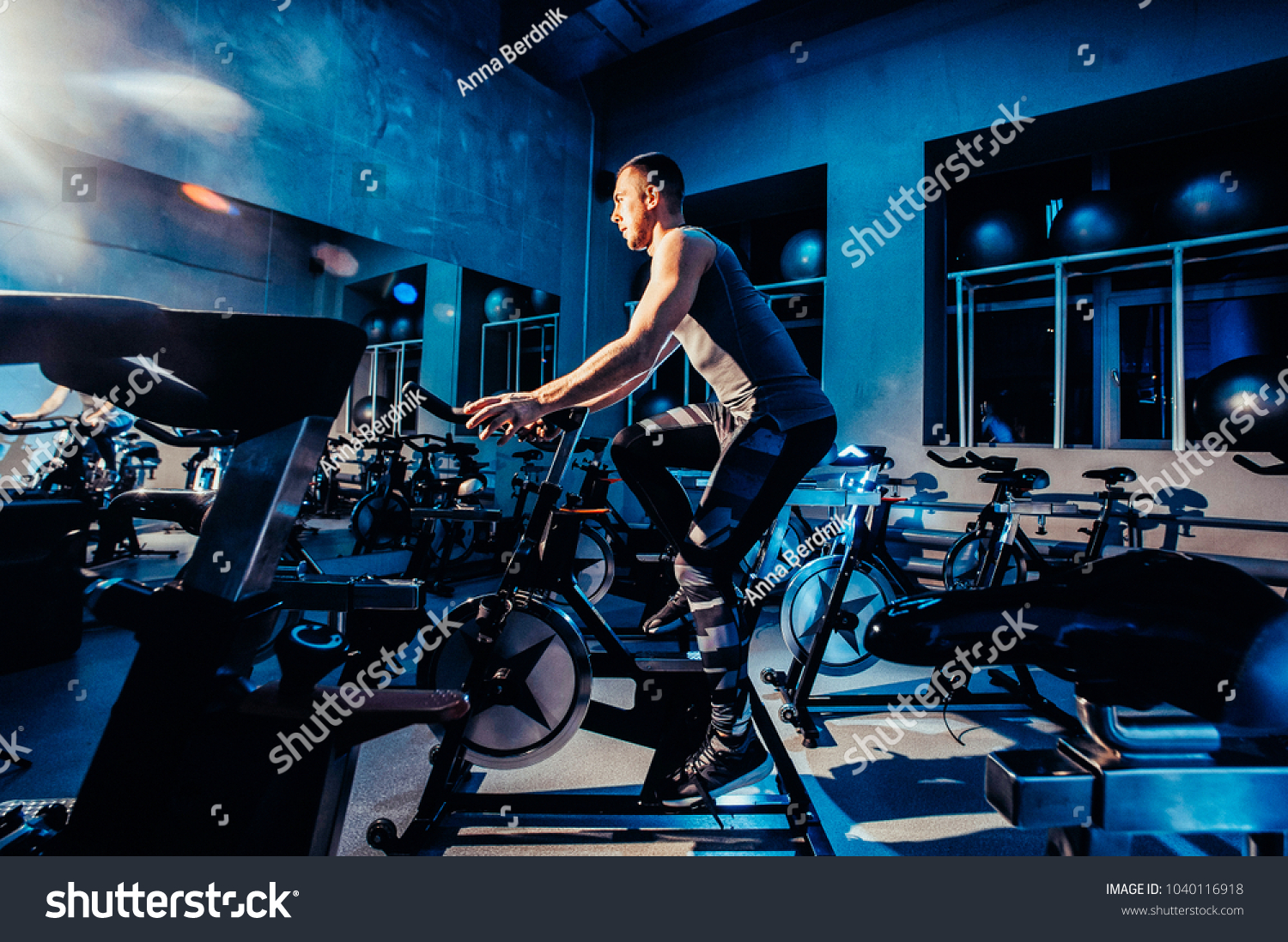 The guy is engaged in a bicycle simulator in the gym. Toned image. The guy is exercising on a stationary bike #1040116918