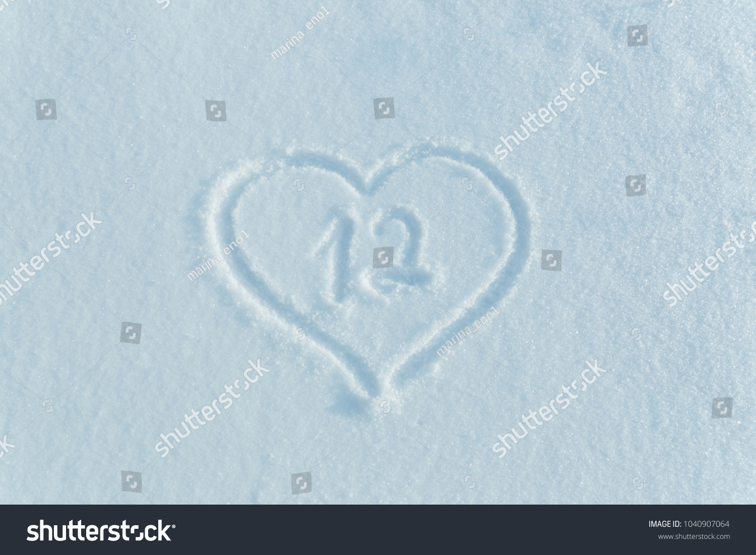 The number twelve drawn on the snow surrounded by a frame in the form of a heart.  #1040907064