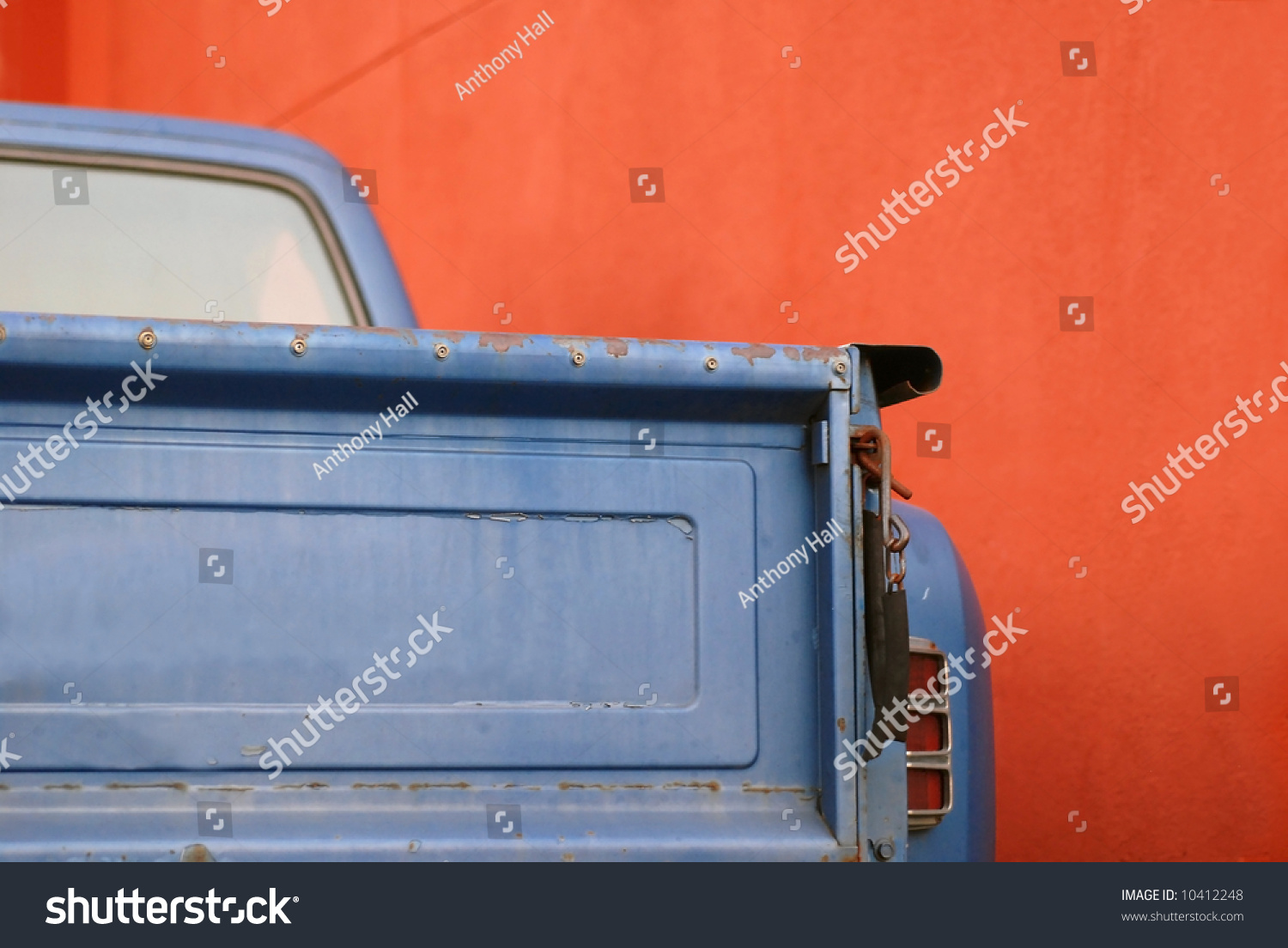 The tailgate of a blue battered sixties American Pickup Truck in front of a red wall #10412248