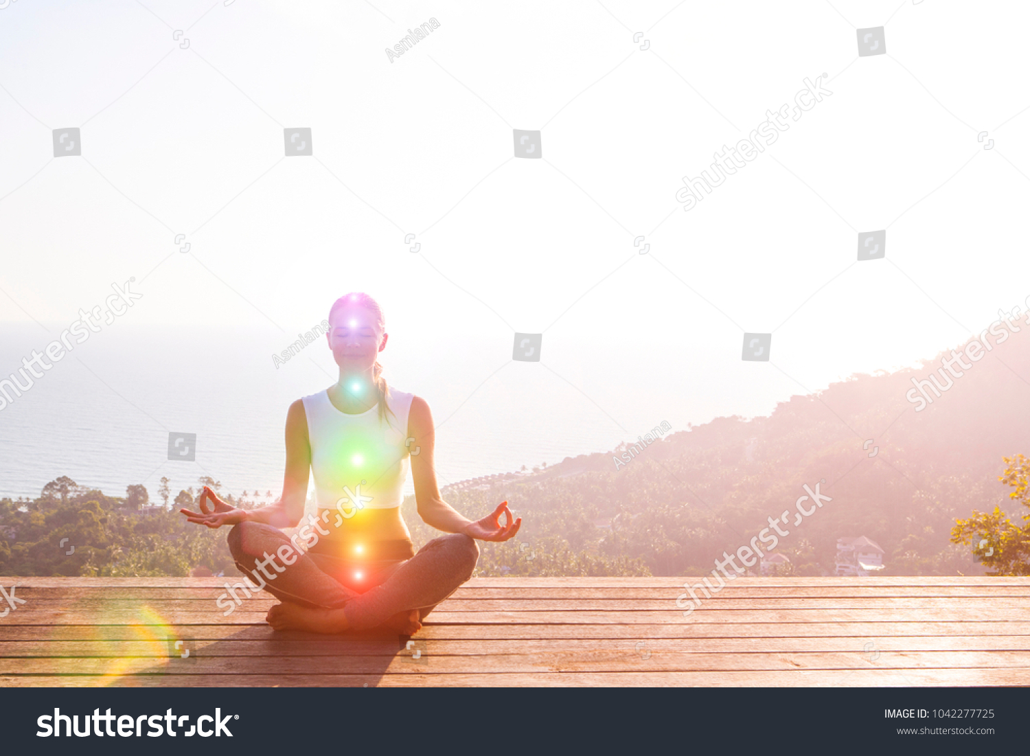 Beautiful woman sits in a pose of a half lotus on high place amazing view of the island outside, she practicing yoga meditation glowing seven all chakra eyes closed calm. Kundalini energy #1042277725
