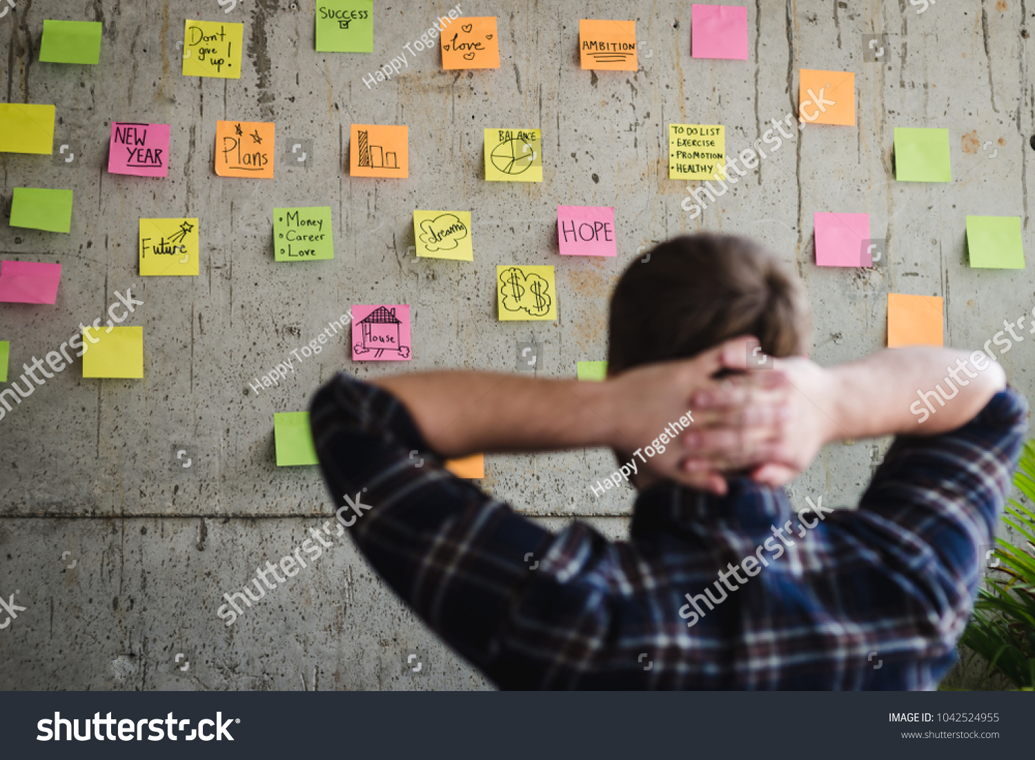 Back of entrepreneur sitting in office and look at colorful sticky message on cement wall. Work lifestyle concept.  Selective focus. #1042524955