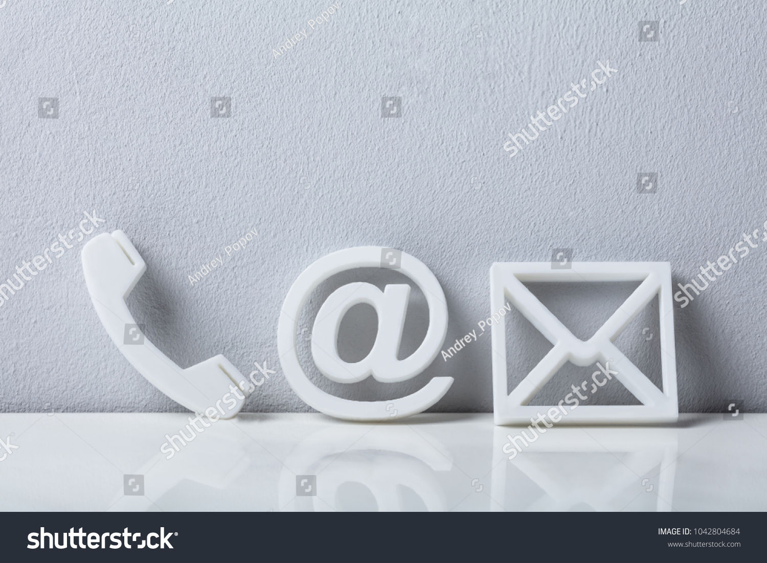 Contact Methods. Close-up Of A Phone, Email and Post Icons Leaning On White Wall #1042804684