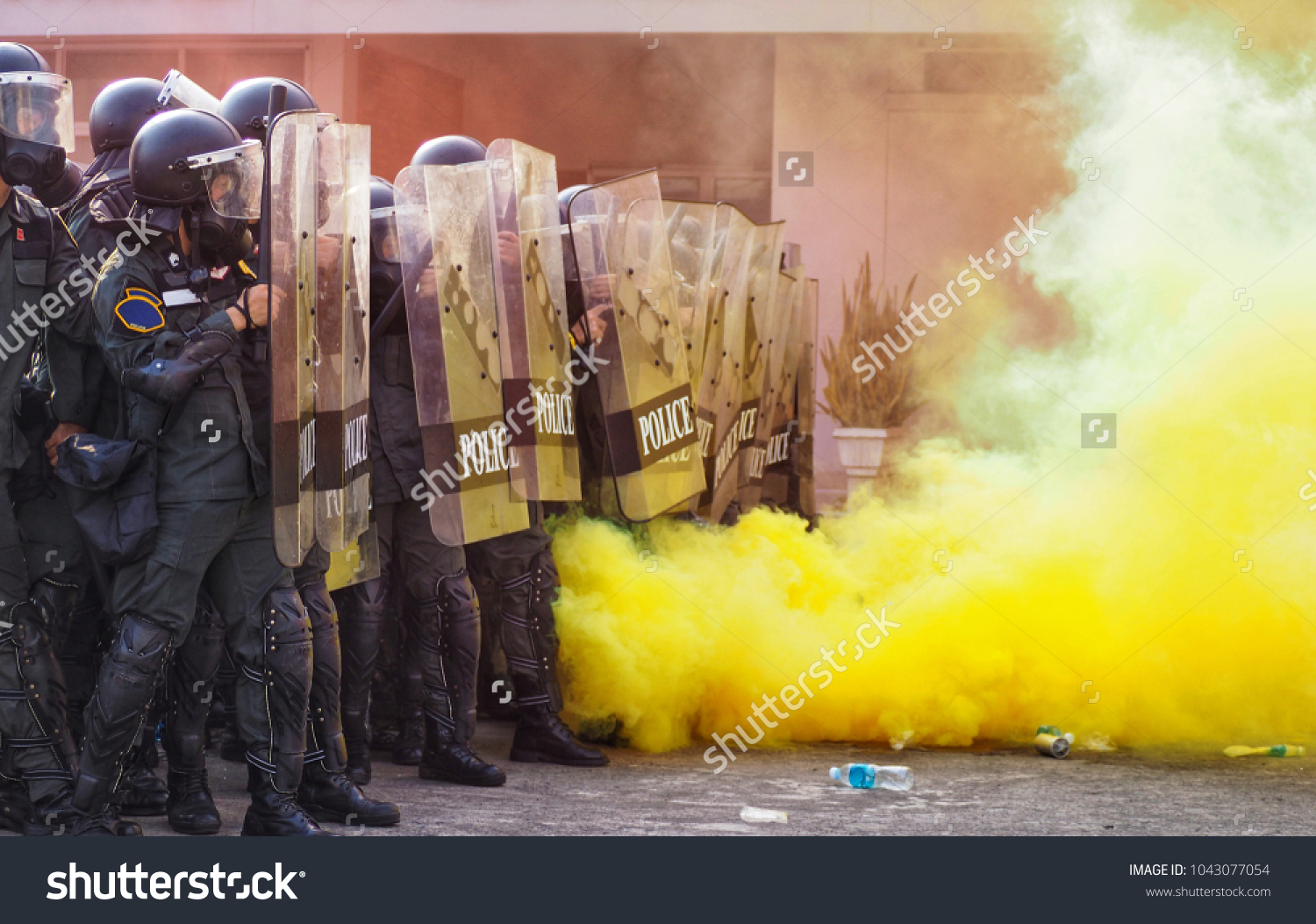 Group riot police with protective gear and shields surrounded by tear gas and yellow color smoke bomb in tactical training #1043077054