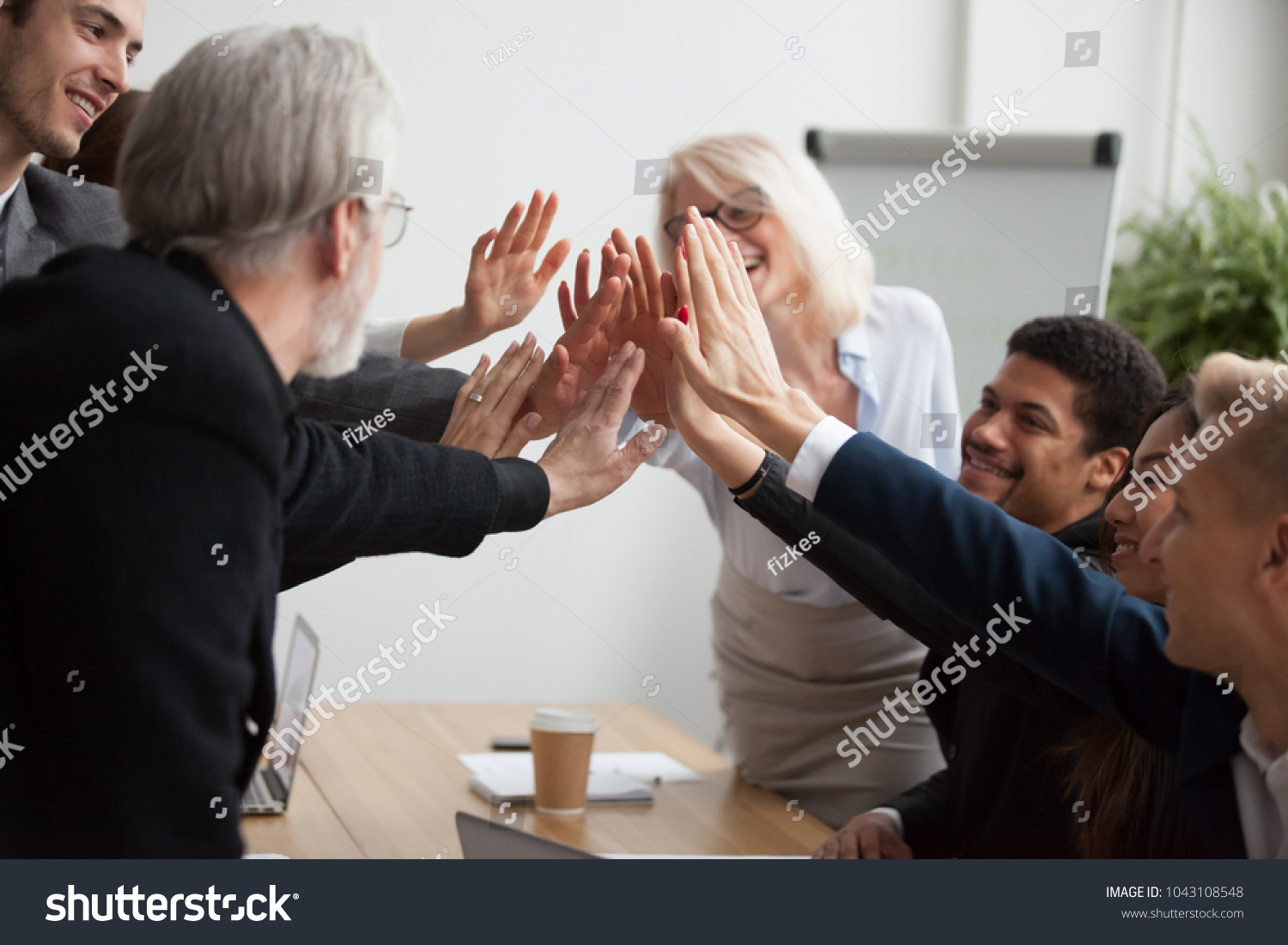 Multiracial young and senior business people join hands giving high five together, motivated diverse team showing team spirit synergy in goal achievement, promising help, supporting unity in teamwork #1043108548