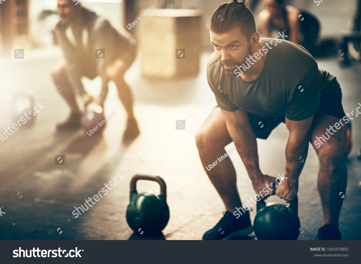 Fit young man in sportswear focused on lifting a dumbbell during an exercise class in a gym #1043370892