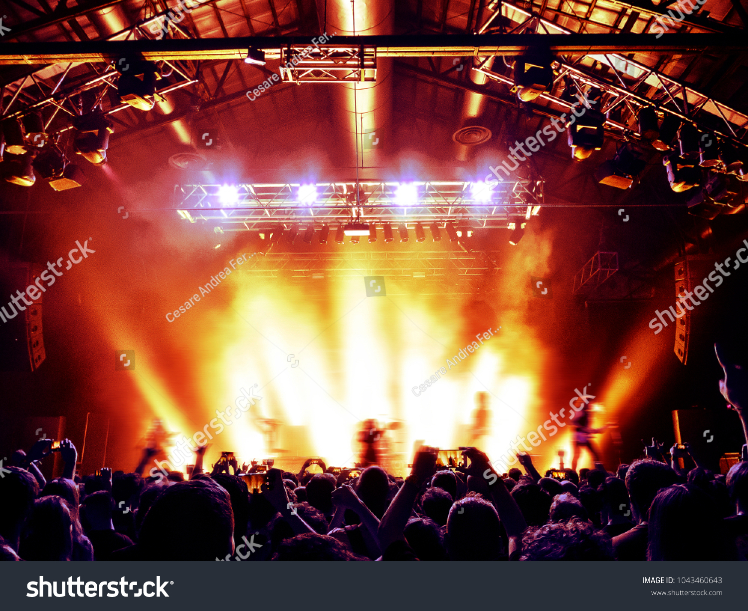 Concert hall with a lit stage and people silhouettes during a concert #1043460643