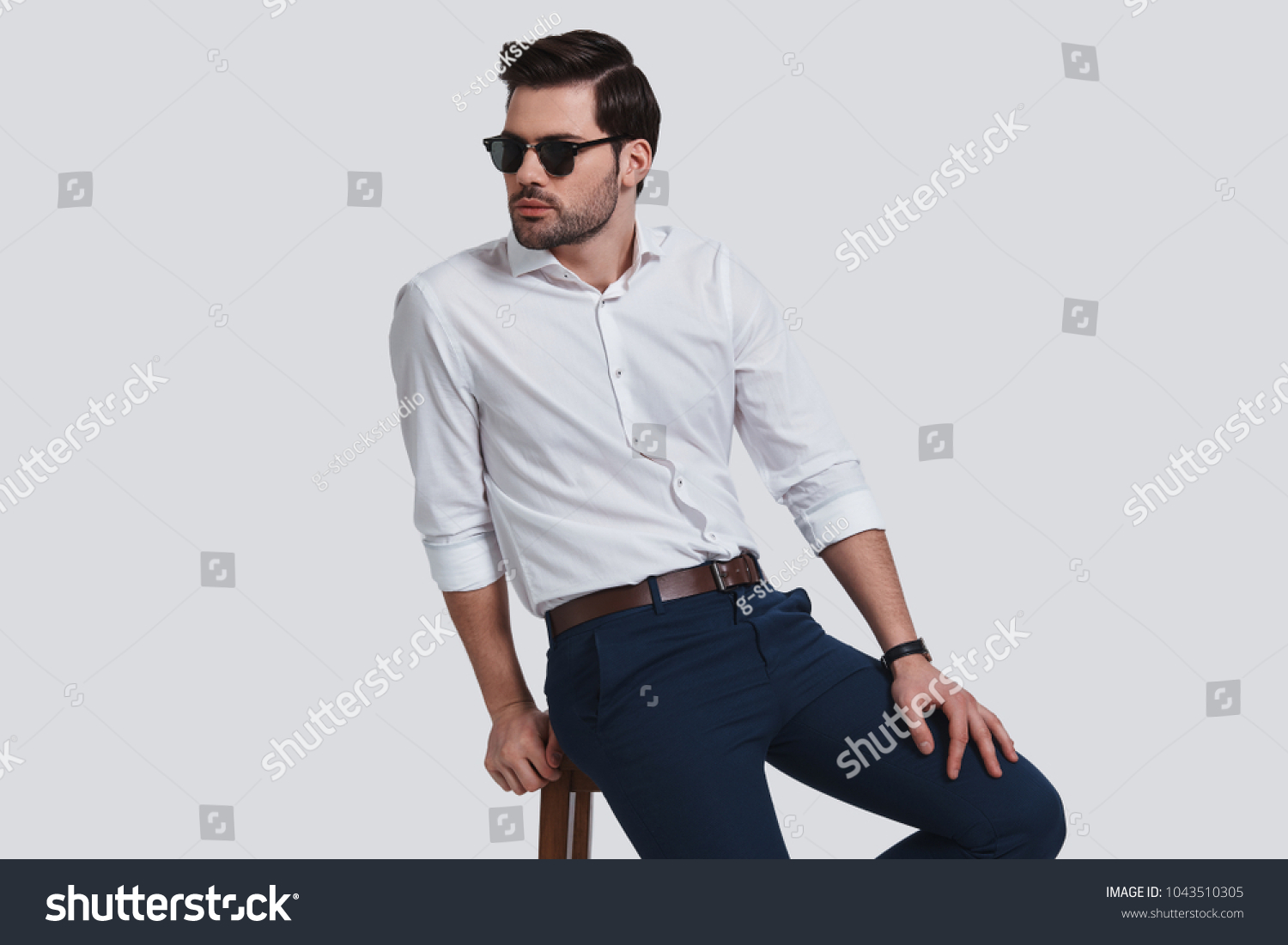 Totally handsome. Good looking young man in eyewear looking away while sitting against grey background #1043510305