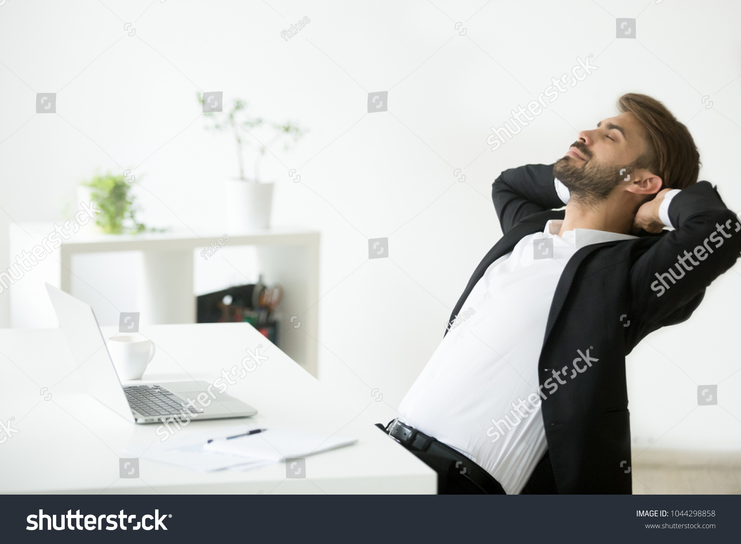 Successful young businessman in suit relaxing at workplace with laptop finished work, relaxed calm employee feels happy breathing fresh air, smiling ceo enjoys break in office, no stress free relief #1044298858