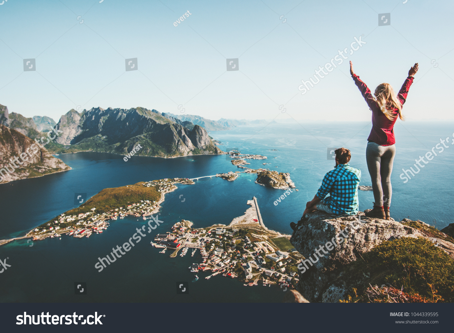 Couple family traveling together on cliff edge in Norway man and woman lifestyle concept summer vacations outdoor aerial view Lofoten islands Reinebringen mountain top #1044339595
