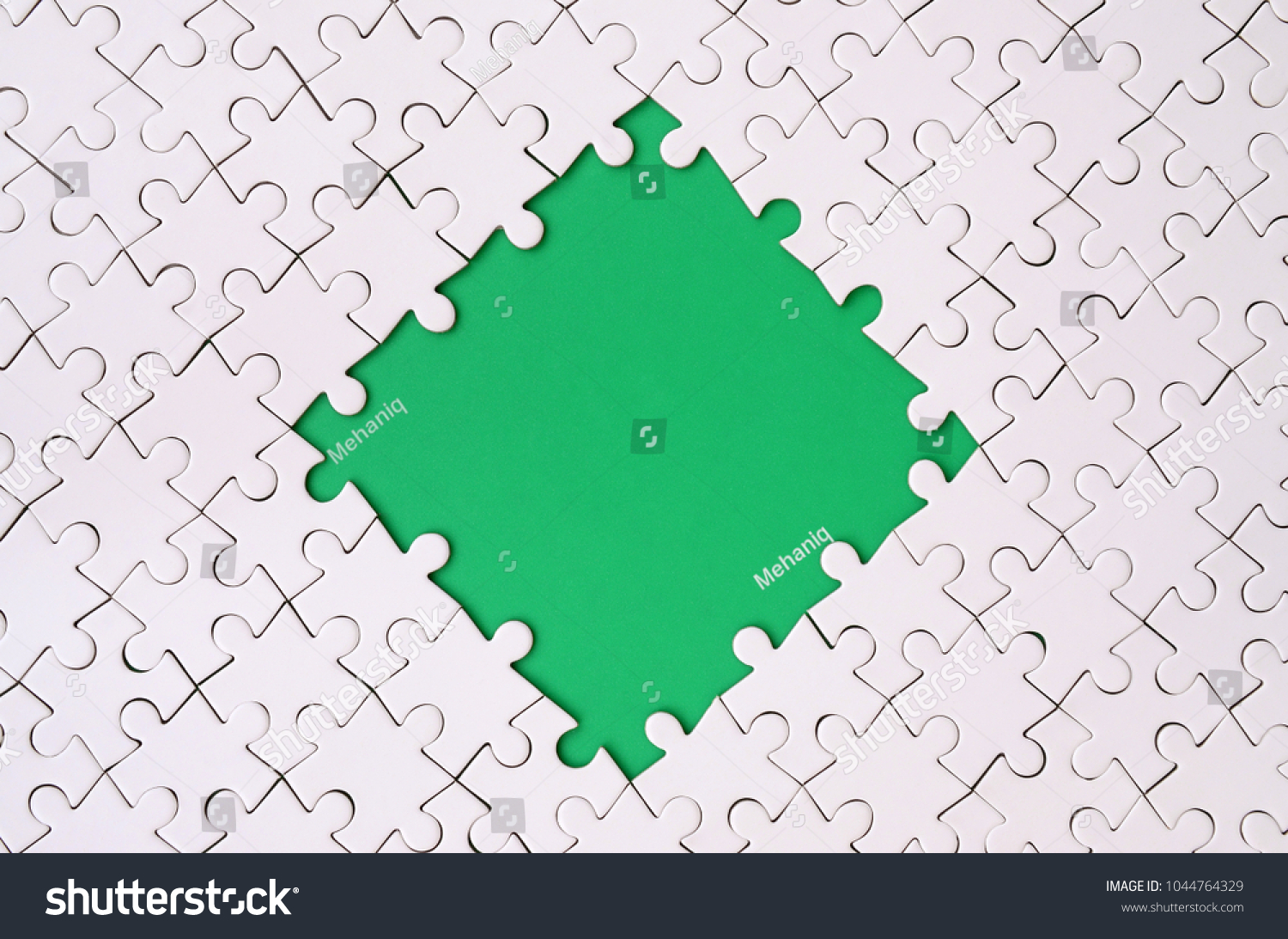 Framing in the form of a rhombus, made of a white jigsaw puzzle around the green space #1044764329