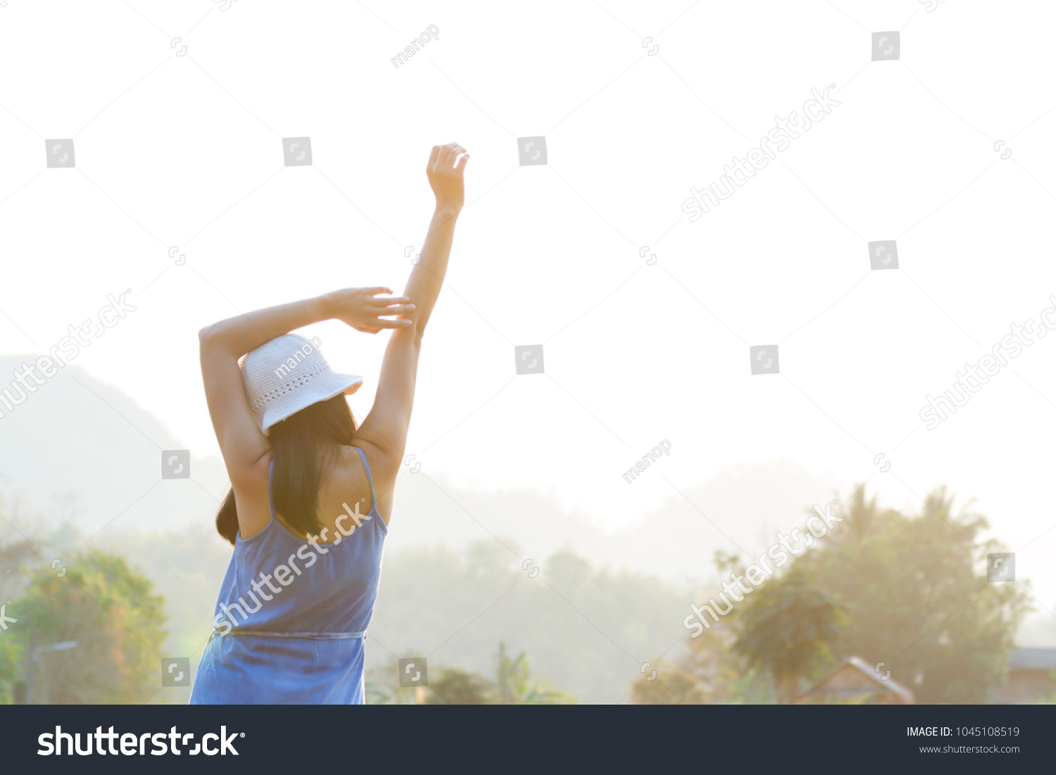 woman standing and rising hands in morning with sun light #1045108519