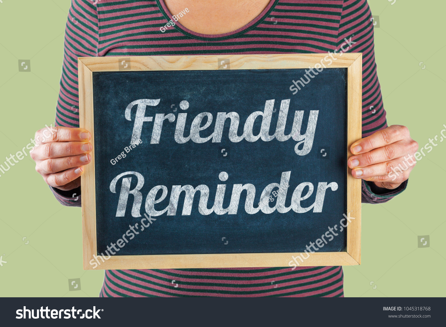 Female hands holding small black chalkboard in front of the body with written words saying Friendly Reminder #1045318768