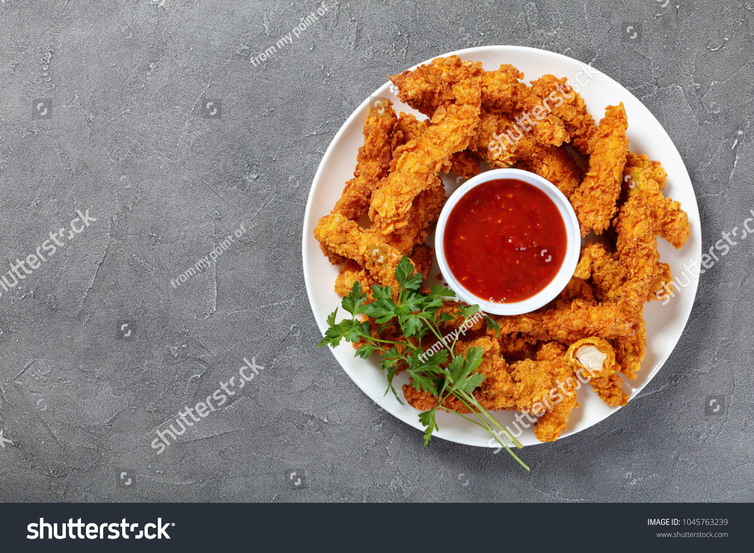 delicious crispy fried chicken breast strips  with tomato sauce on white plate, on concrete table, view from above #1045763239