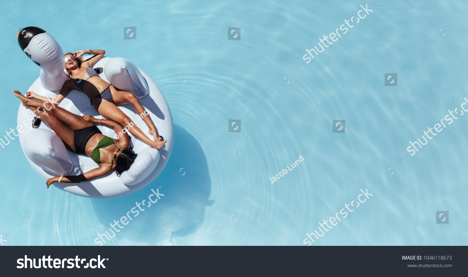 Top view of female friends wearing bikini lying on an inflatable toy in pool. Woman sunbathing on floating pool inflatable toy. #1046118673