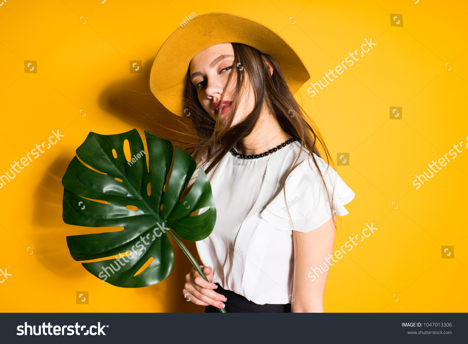 confident young long-haired girl model in a fashionable hat holds a green leaf and poses #1047013306