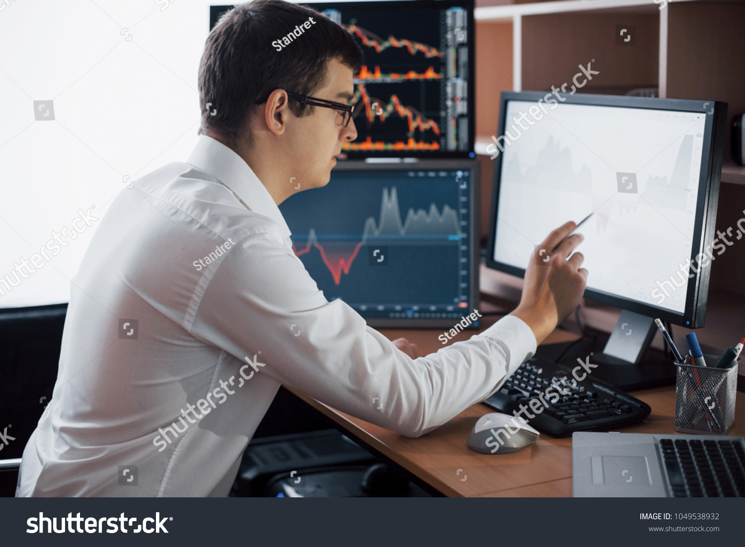 Busy working day. Close-up of young businessman looking at monitor while sitting at the desk in creative office. #1049538932