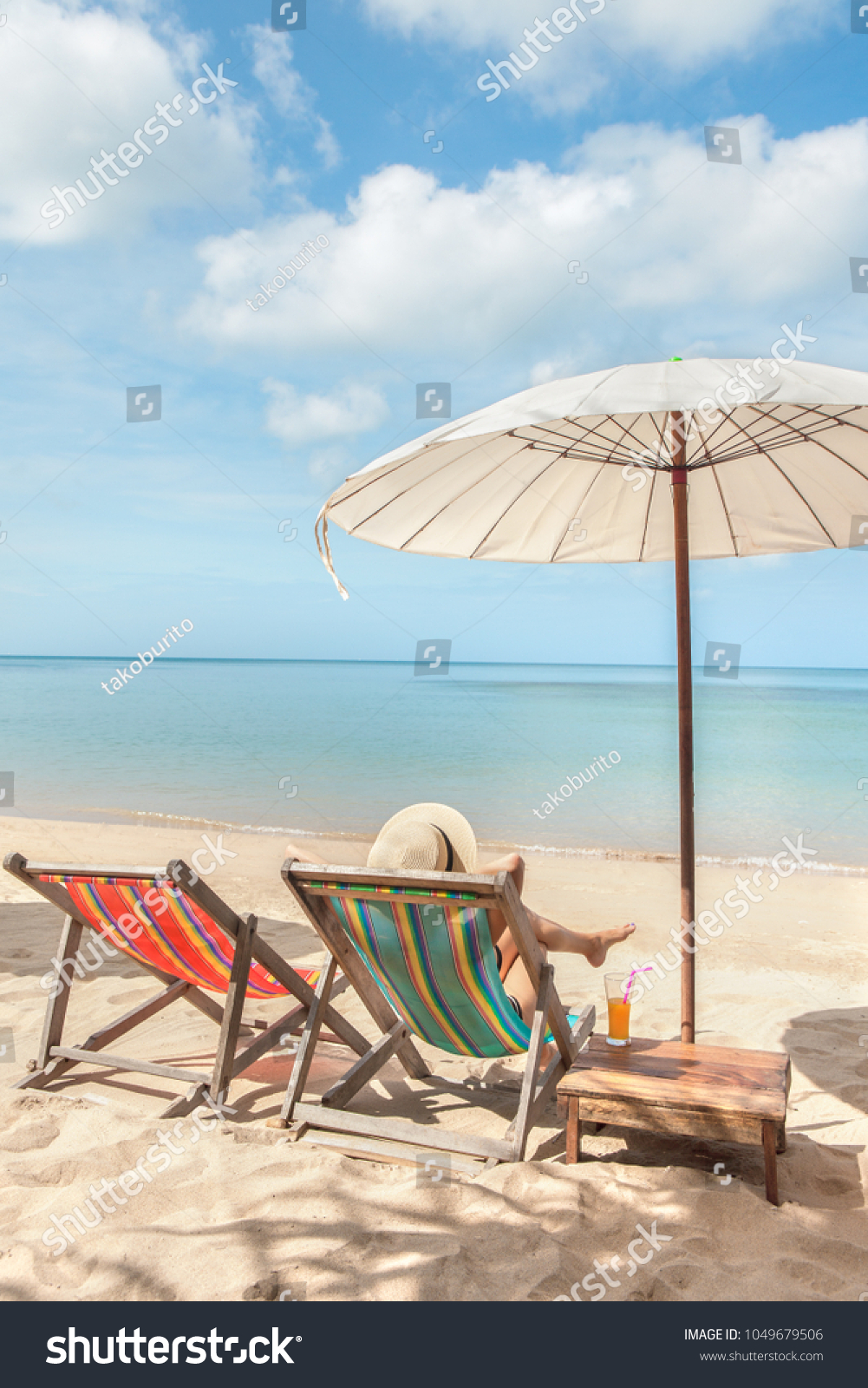 Woman at beautiful beach sitting on chaise-lounge and drinking cocktail top view #1049679506