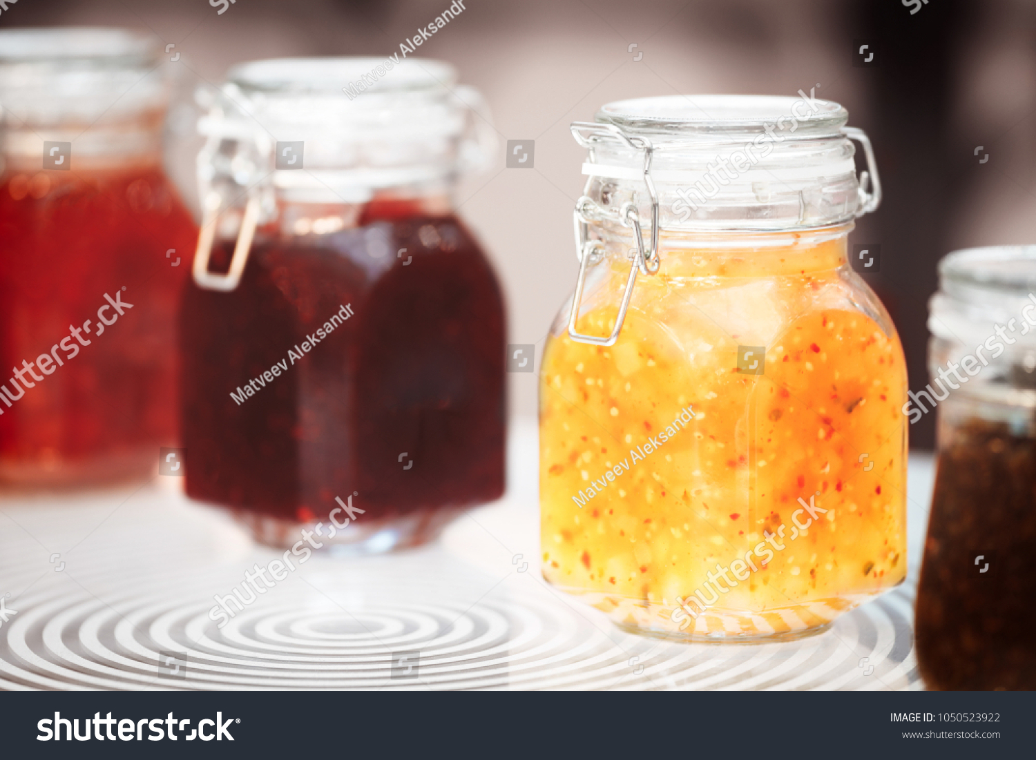 Close-up row of several glass with red yellow orange jars jam conserve confiture pozzy on table, breakfast concept, kitchen background, healthy eating concept, conservation concept. #1050523922