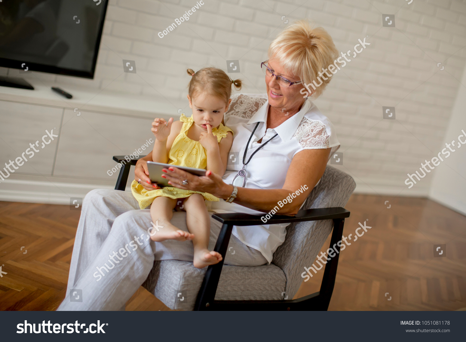 Grandmother reading book to little granddaughter in the room #1051081178