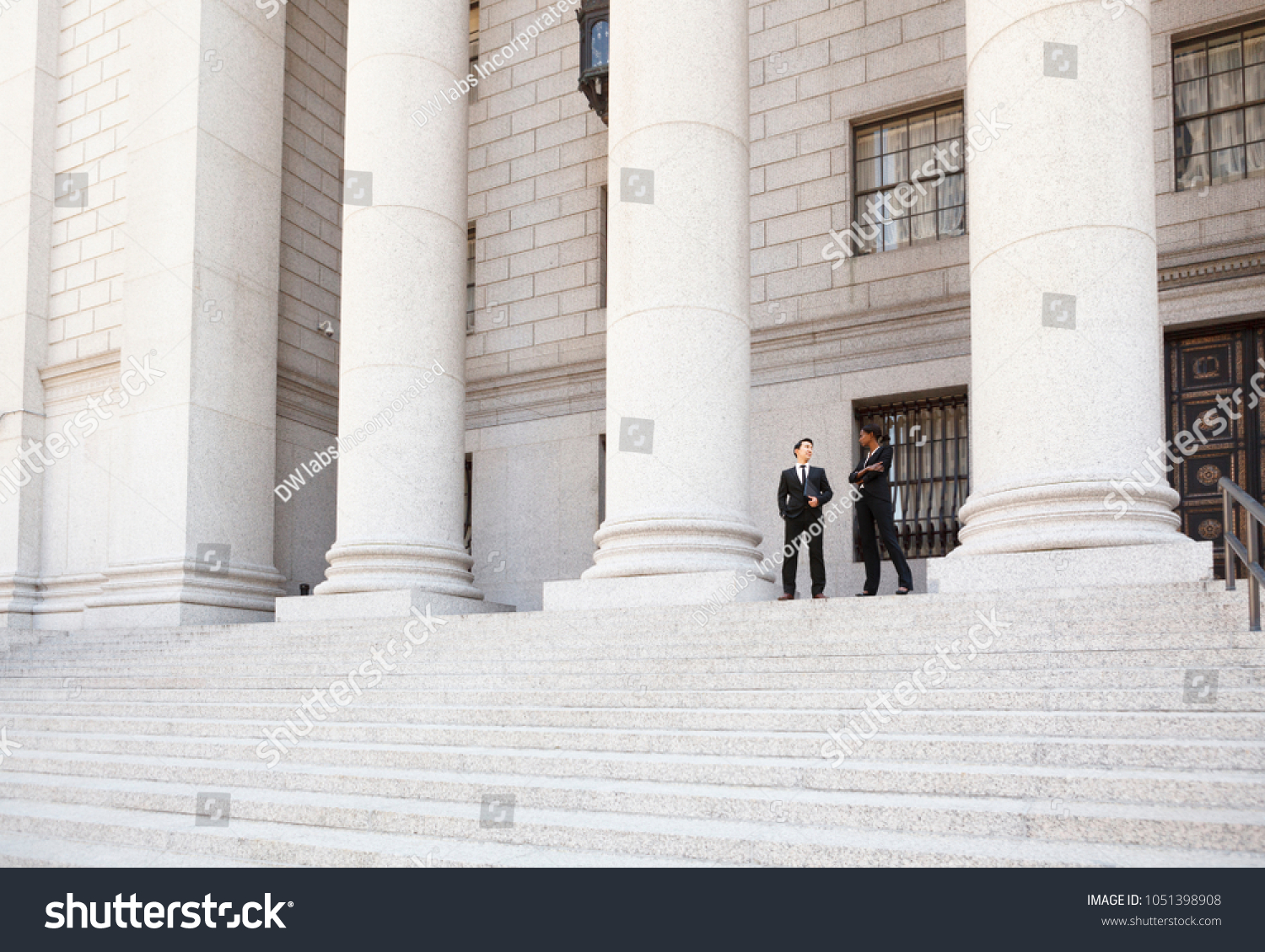 A well dressed man and woman converse on the steps of a legal or municipal building. Could be business or legal professionals or lawyer and client. #1051398908