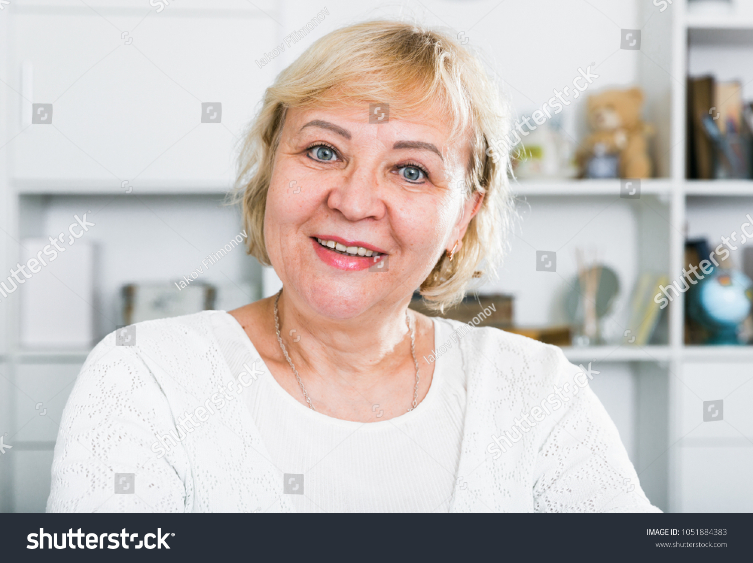 Mature woman sitting at table at home and looking at camera #1051884383