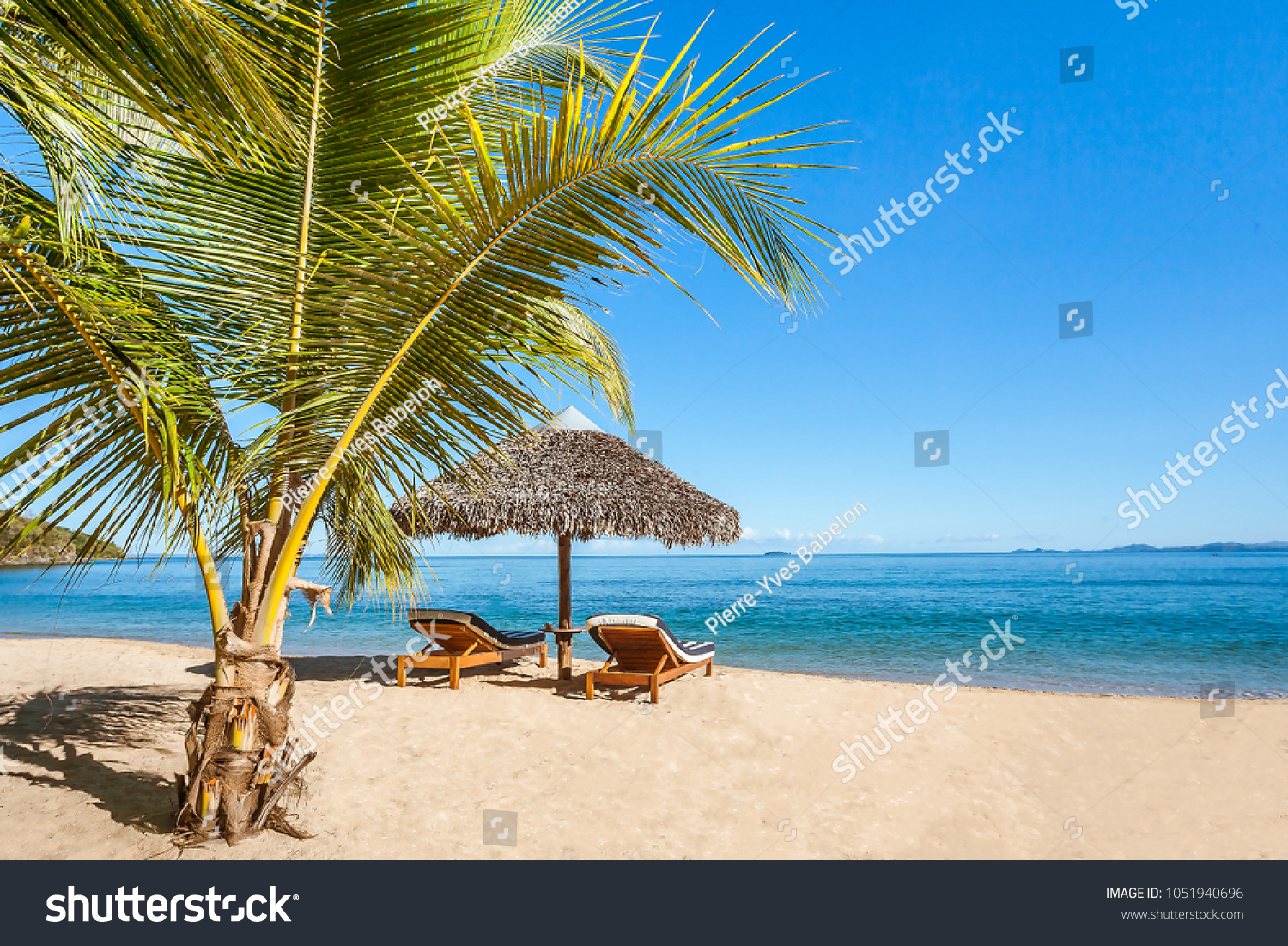 Two sunbeds under a straw umbrella on the tropical beach of Nosy Be, Madagascar #1051940696