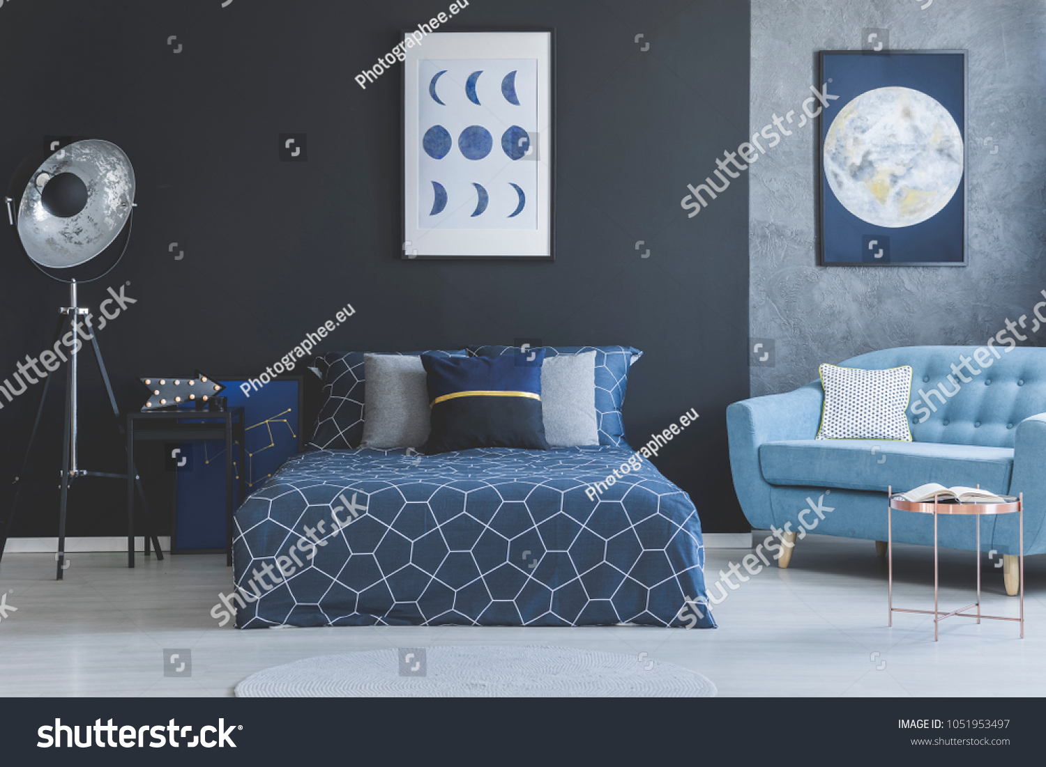 Blue sofa in bedroom interior with navy blue bed against dark wall with gallery of posters #1051953497