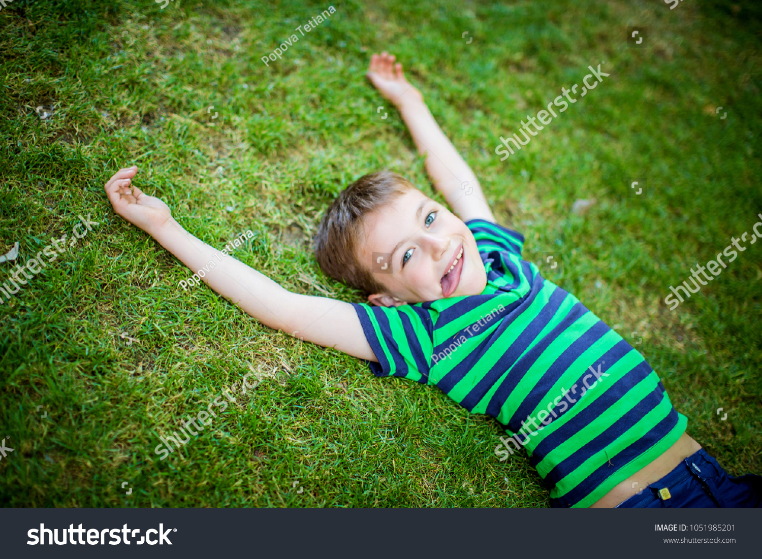 Little happy boy lies on the green grass #1051985201